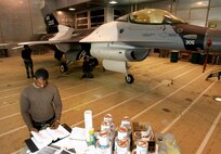 KUNSAN AIR BASE, South Korea --  Staff Sgt. Cory Goines, thumbs through a technical order manual for finishing instructions while Senior Airmen Kevin Stevens and Matt Wuensch, take care of the final details on a newly painted arctic scheme F-16 aircraft here Nov 30.  Sergeant Goines and Airmen Stevens and Wuensch, are Aircraft Structural Maintenance Journeymen with the 8th Maintenance Squadron.  The 8th MXS painted the aircraft in preparation for an upcoming Eielson/Kunsan F-16 swap. The aircraft is the first unit to have an arctic scheme.  (U.S. Air Force photo/ Tech. Sgt. Quinton T. Burris)