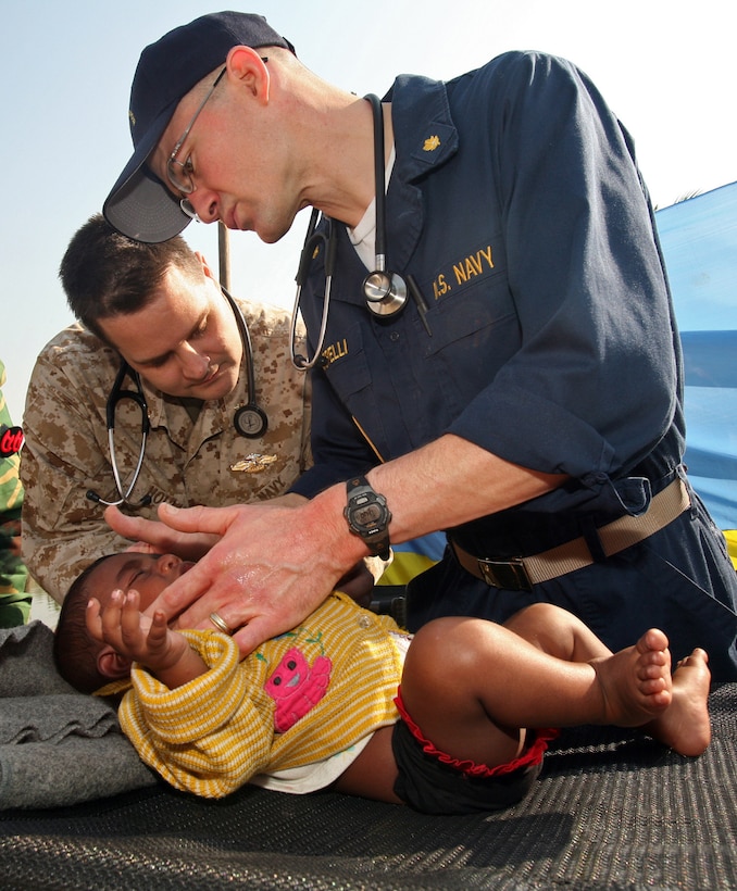 Navy Lt. Cmdrs. Trey Hollis, left, chief surgeon of the 22nd Marine Expeditionary Unit (Special Operations Capable) command element, and Lou C. Cimorelli, the ward officer of USS Kearsarge, provide medical aid to a child in South Khali, Bangladesh, Nov. 28, 2007. Kearsarge and the 22nd MEU are providing humanitarian relief to the area following Tropical Cyclone Sidr, which struck the country\'s southern coast Nov. 15, 2007, killing more than 3,000 people and leaving thousands more homeless. Photo by Cpl. Peter R. Miller, USMC