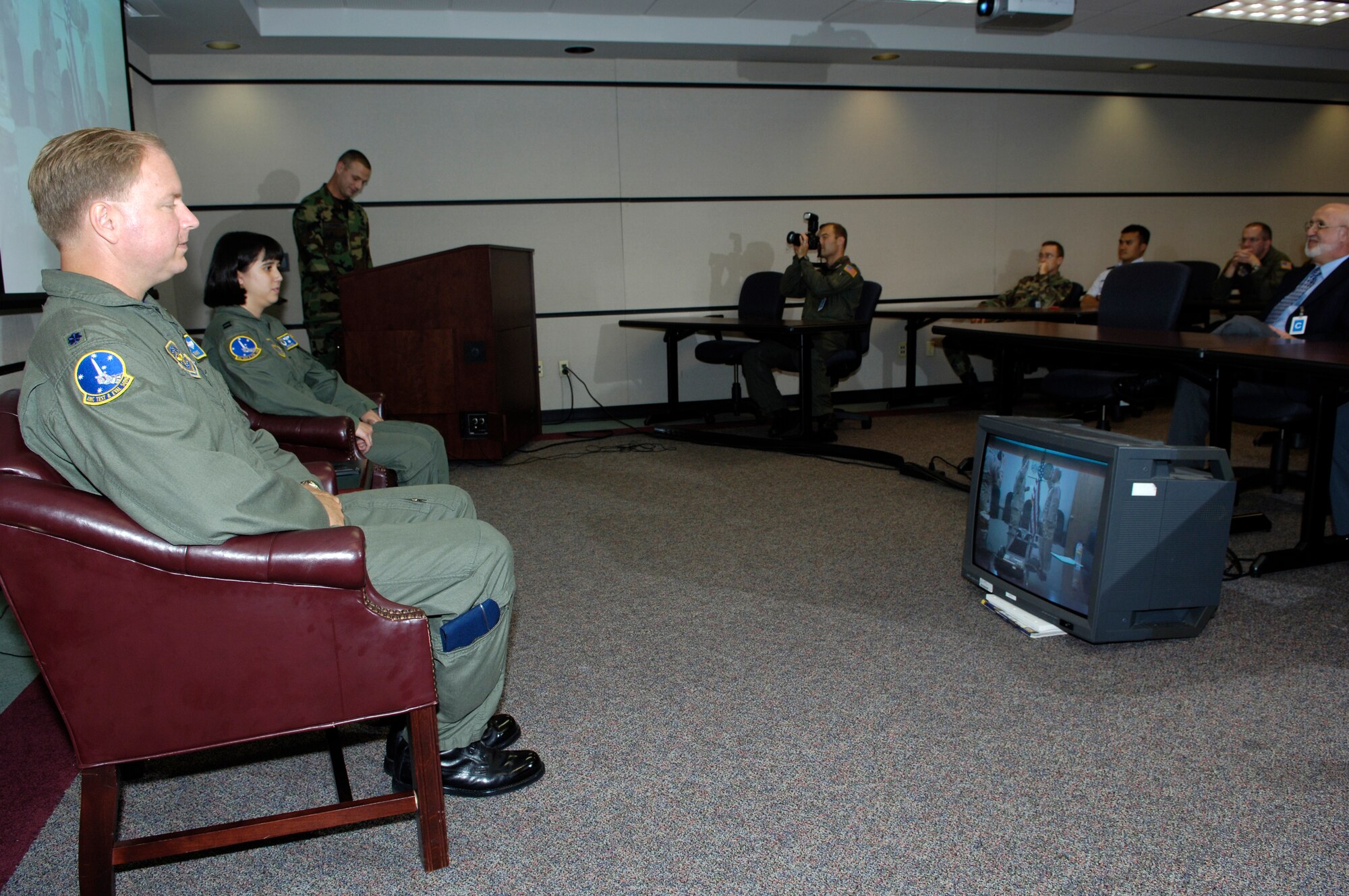 Lt. Col. Tim White, Air Mobility Command Test and Evaluation Squadron commander, and Capt. Carmilla Tatel, AMC TES logistics flight commander, watch a monitor of her husband, Capt. Merwin Tatel, Headquarters AMC Air Intelligence Squadron, operating at the U.S. Air Force Expeditionary Center, pin on major. The captains' had their pin-on ceremonies via a video teleconference hookup. Capt. Merwin Tatel is currently deployed to Southeast Asia. (U.S. Air Force photo/Kenn Mann)