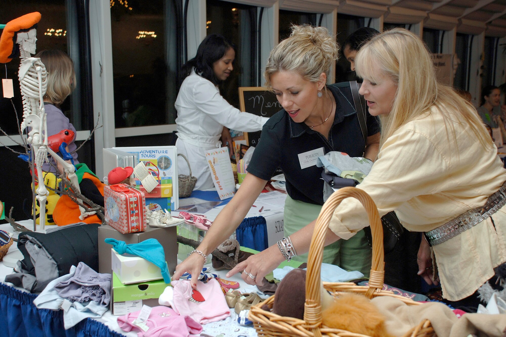 From right, Laura Hoene points out a variety of baby outfits to Cindy Canavan during the Hanscom Spouses’ Club kick-off event Sept. 25 at the Minuteman Club. The theme of the event was, “Common Ground: Together we’re better.” (U.S. Air Force photo by Jan Abate.)