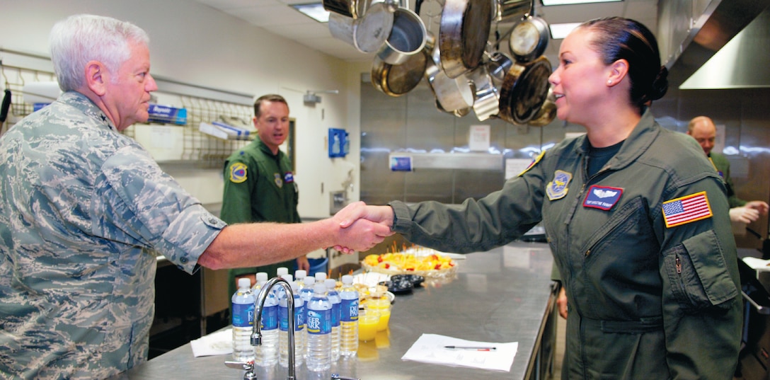 Tech. Sgt. Khristine Farmer, 1st Airlift Squadron flight attendant shakes hands with Gen. Arthur Lichte, commander, Air Mobility Command, as Lt. Col. James Mercer, 1AS commander, observes during a tour of the flight attendant kitchen, Sept. 28. (US Air Force/A1C Renae Kleckner)