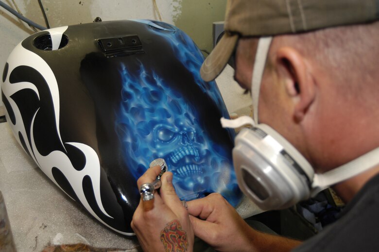 Sergeant Long airbrushes a skull with true fire. He uses a white flame-design tape to help him during the first stage of airbrushing. Not only does he pinstripe the fenders, he also designs and carves out the fenders.  (U.S. Air Force photo/Airman Shen-Chia Chu)                             