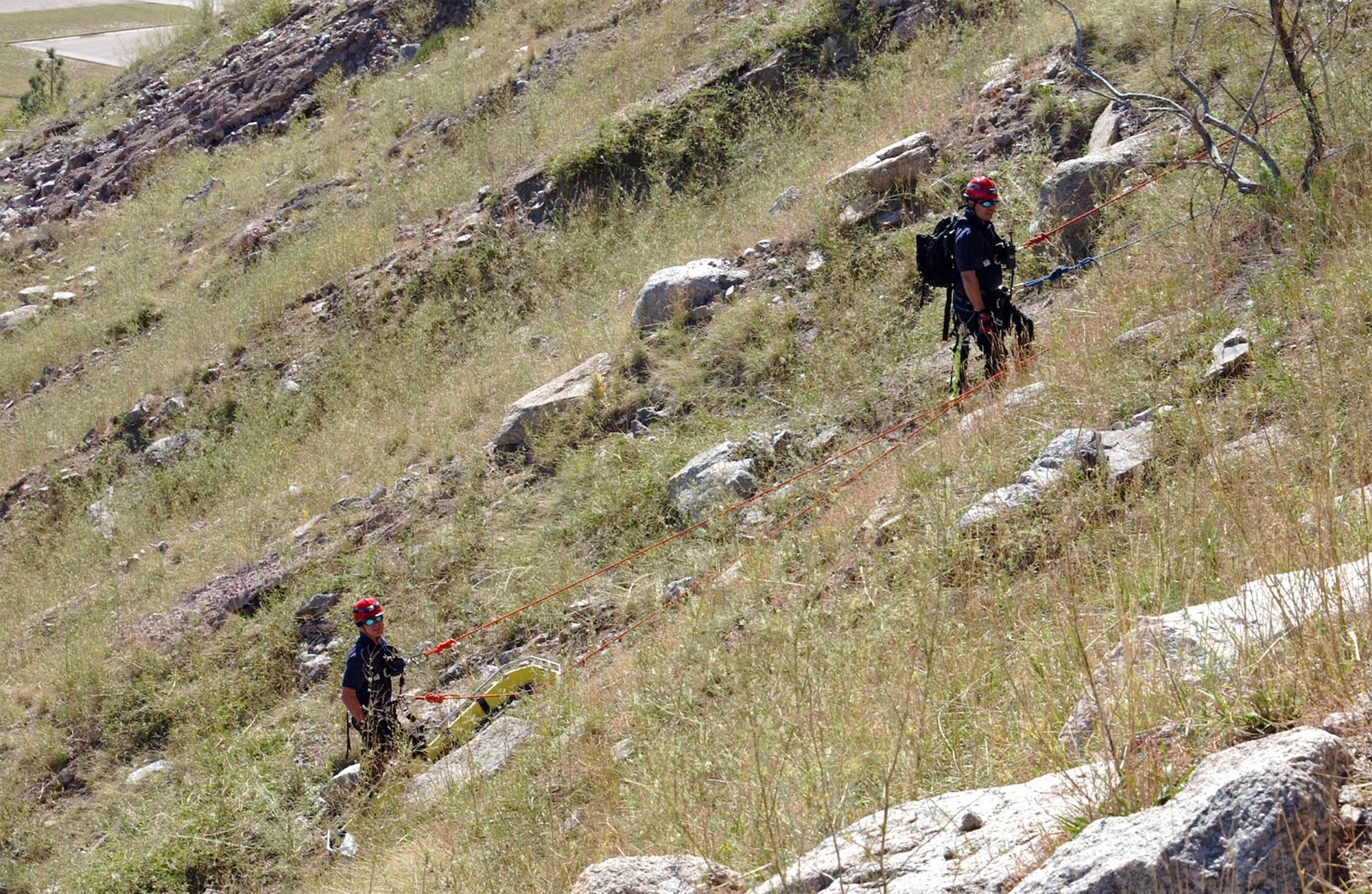 Firefighters at Cheyenne Mountain AFS perform practice rescues on a steep hill. Firefighters on the mountain must stay in top physical condition to complete their everyday tasks, which can range from rappelling down steep ravines during rescues to running to the scene of a fire – all at an altitude of more than 7,000 feet. (U.S. Air Force photo)