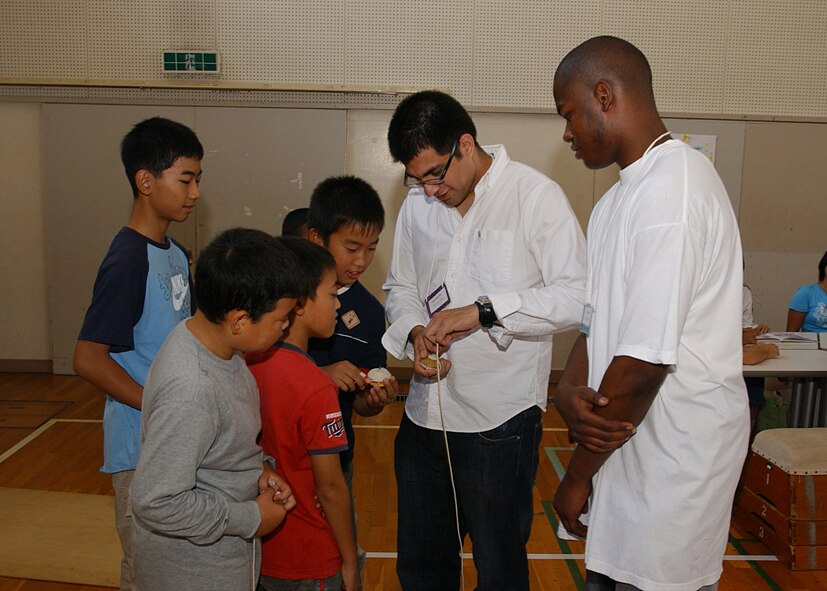 FUSSA, Japan - Students from Fussa Fourth Elementary School show Staff Sergeant Anthony Ruy and Senior Airman Michael Mitchell, both from the 374th Maintenance Squadron, how to wrap the string around a top during the Fussa Elementary Exchange program on October 4, 2007. Volunteers from Yokota Air Base, Japan visited the school and were given the chance to interact with a group of 6th graders and learn about their culture through various workshops set up by the students. (U.S. Air Force photo by Airman First Class Jonathan Fowler)