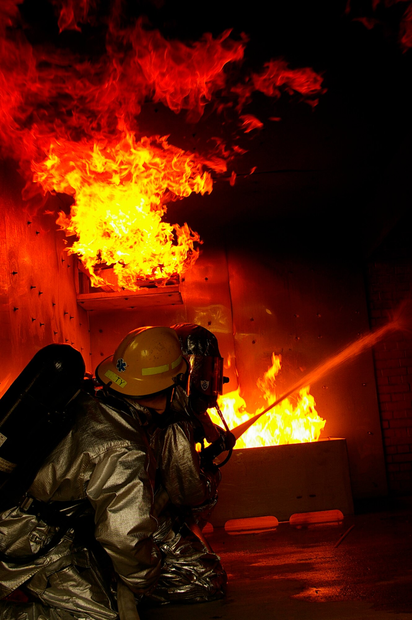 Gethin Jones, right, presenter of classic children's television programme, Blue Peter, helps Tech. Sgt. Rick Henderson, 100th Civil Engineer Fire Department, put out a fire in the smoke-house at RAF Mildenhall Oct. 1. The presenter and a camera crew visited the RAF Mildenhall Fire Department Oct. 1 and 2. Gethin spent two days with U.S. Air Force and Ministry of Defence firefighters, being trained by, and working alongside his firefighter buddy, Sergeant Henderson, when he and a camera crew came to record Gethin's two days as a firefighter for a special item on an upcoming edition of Blue Peter. The presenter, who is currently starring in "Strictly Come Dancing," worked with Green Watch and Blue Watch MoD firefighters, and U.S. military firefighters. He was put through his paces when he performed tasks such as a hose pull, mannequin drag, cutting up cars, and putting out fires on a simulated aircraft -- all while wearing a protective clothing and equipment weighing between 70 to 100 pounds. (U.S. Air Force photo by Karen Abeyasekere)