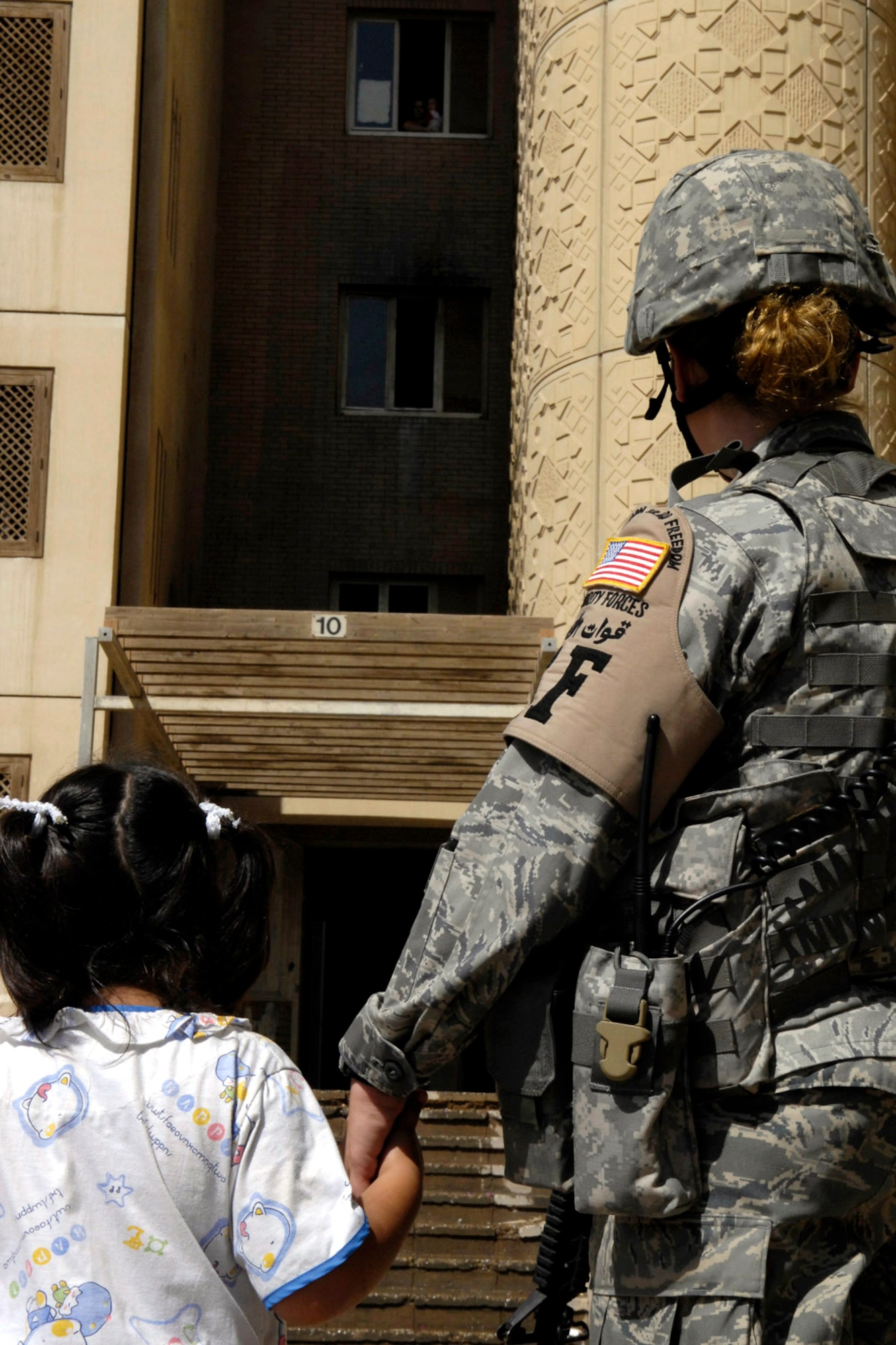 Airman 1st Class Jessica Gallaway, deployed from Grand Forks Air Force Base, N.D., assigned to the 732nd Expeditionary Security Forces Squadron, Det. 4, holds an Iraqi girl's hand as they wait to return her to her apartment after a fire. Air Force security forces are the first responders for the international zone, Baghdad, Iraq. They are in-lieu-of tasking, meaning they are filling an Army billet on six-month deployments. (U.S. Air Force photo/Staff Sgt. Angelique Perez) 
