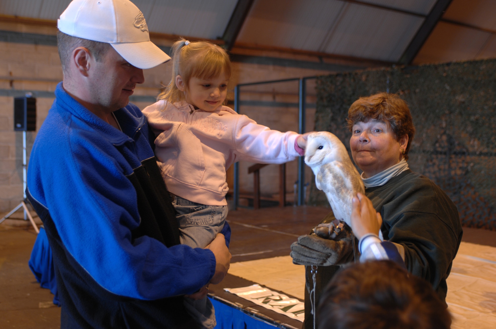 Staff Sgt. Matthew Rowan, from the 100th Aircraft Maintenance Squadron, and his daughter Cora Rowan get some up close time with Jack a barn owl while Pat Kitchen from the Raptor Foundation explains a little about Jack and other barn owls. The Raptor Foundation was just one of many displays at the Lakenheath Holiday Bazaar an annual event held by the Lakenheath Officer and Civilian Spouses club and Enlisted and Civilian Spouses club. (U.S. Air Force photo by Staff Sgt. Christopher Campbell)
