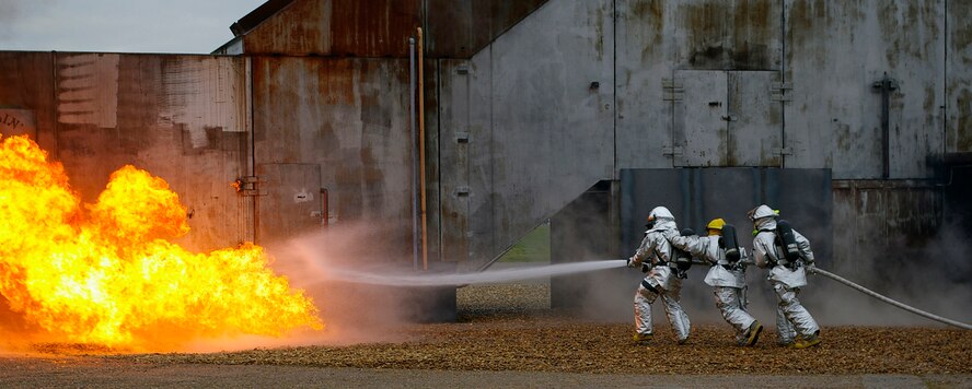 Gethin Jones, left, Tech. Sgt. Richard Henderson, center, 100th Civil Engineer Squadron Fire Department, and Staff Sgt. Douglas Shimmin, also 100th CES Fire Department, sweep water from the pressurized hose across the flames, to put out the fire on the simulated aircraft Oct. 2. Gethin Jones, presenter of children's TV program, "Blue Peter," was at RAF Mildenhall Oct. 1 and 2, with a camera crew from the BBC, filming for an upcoming edition of "Blue Peter." (U.S. Air Force photo by Karen Abeyasekere)