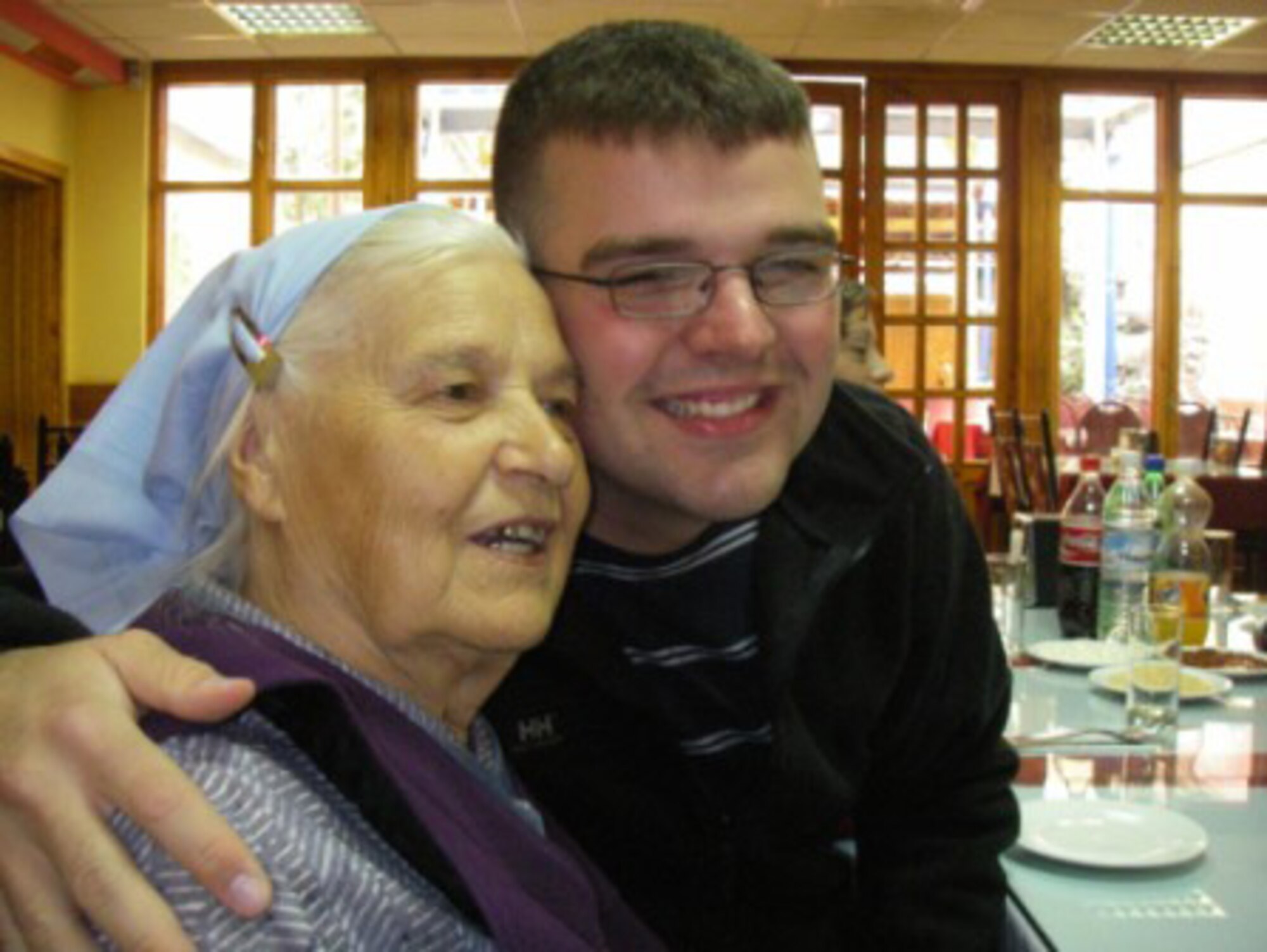 MANAS AIR BASE, Kyrgyzstan--Airman 1st Class Daniel Coomer, 354th Fighter Wing chaplain's assistant, currently deployed to the 376th Air Expeditionary Wing chapel staff, hugs a babushka Sept. 23 at a resturaunt in down town Bishkek, the capital of Kyrgyzstan. Airman Coomer and his coworkers routinely take a group of babushkas to lunch, bring them items such as food and toiletries and give them a $10 stipend per month. The grandmothers live on their own because if they went to a nursing home in Kyrgyzstan, they would be mistreated, the Manas AB chapel staff helps them live on their own. The babushkas are one of 10 different organizations the Manas chapel staff contribute to on a regular basis, to include multiple orphanages and community-oriented organizations. (courtesy photo)