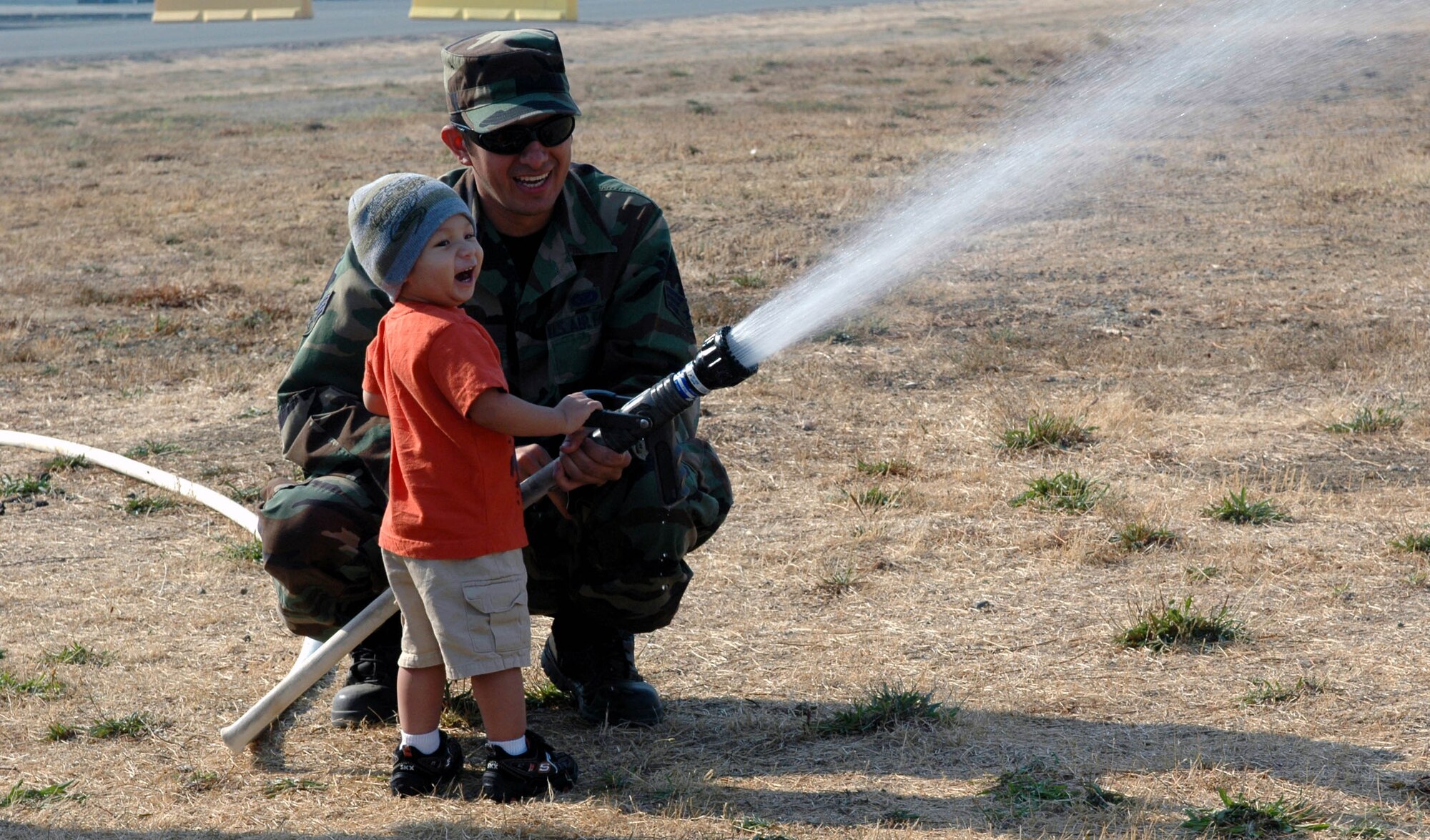 A KUDOS deployer and a Travis firefighter have a little fun with the fire hose during the Kids Understanding Deployment Operations event Oct. 3. Military family members also viewed demonstrations from the 60th Civil Engineer Squadron's Explosive Ordinance Disposal robot, 60th Services Squadron and the 60th Medical Operations Support Squadron. (U.S. Air Force photo/Staff Sgt. Candy Knight)