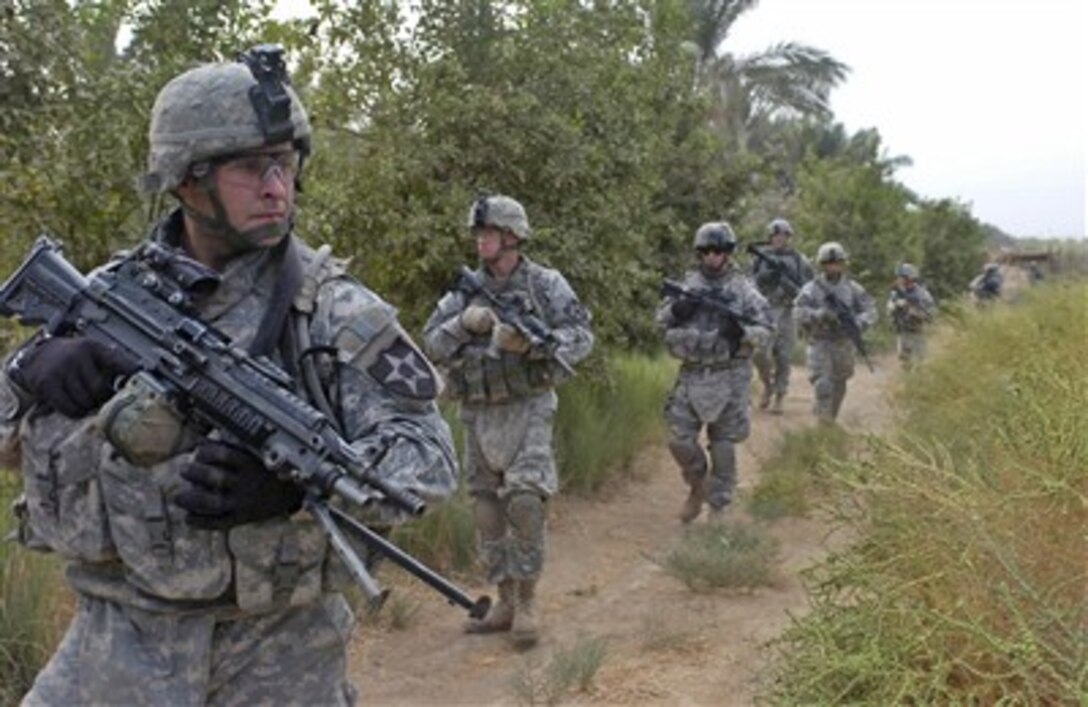 U.S. Army Pfc. Steven Evans (left) and other soldiers patrol through a palm grove near Rashidiyah, Iraq, on Oct. 6, 2007.  Evans is assigned as a machine gunner with Headquarters and Headquarters Company, 4th Stryker Brigade Combat Team, 2nd Infantry Division.  