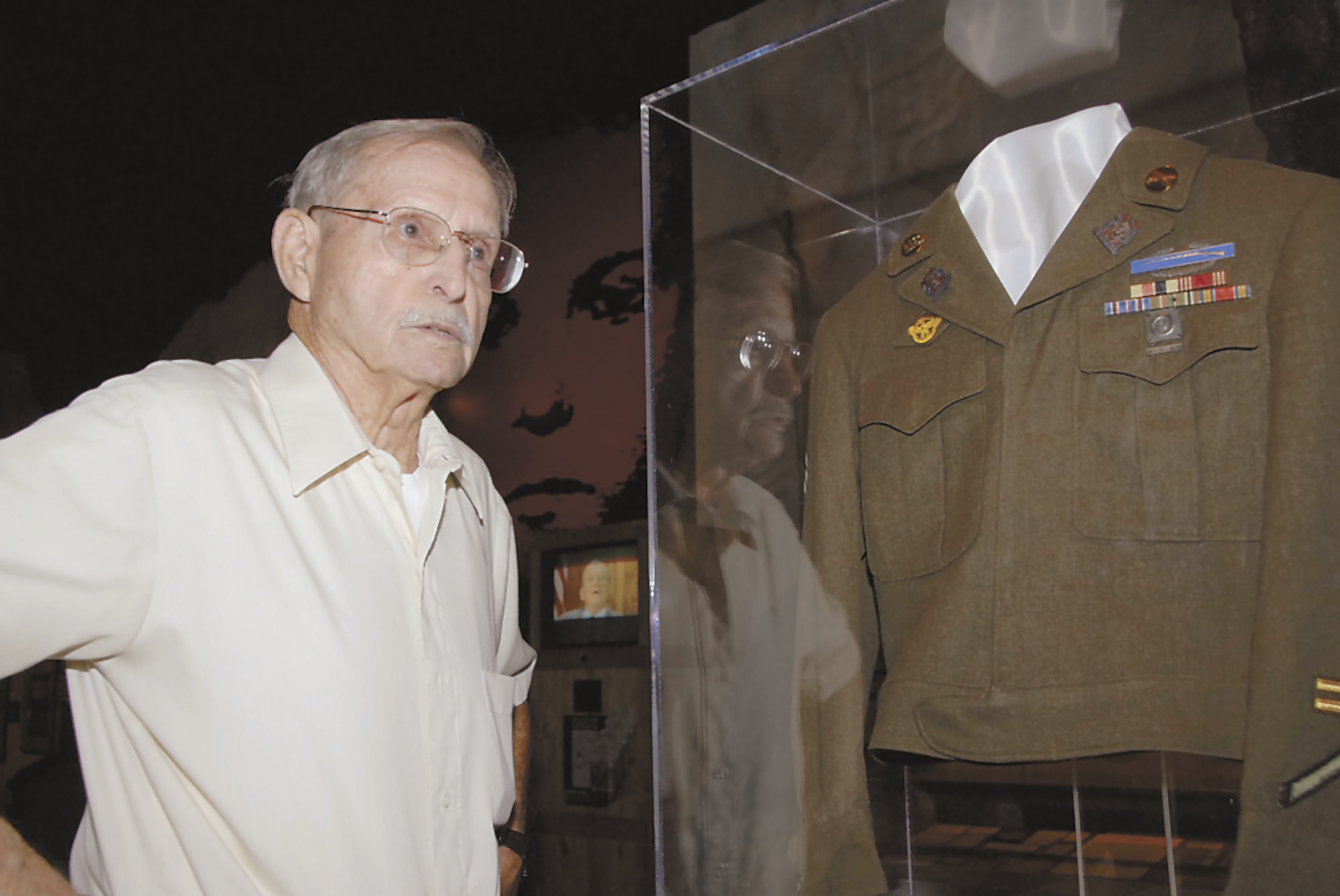 World War II veteran Del Cooper reflects on his time in Germany where his unit helped to liberate Holocaust victims from Nazi camps.  Cooper stands next to a jacket he donated to the National Museum of the U.S. Air Force.  (Skywrighter photo by Christy Web)
