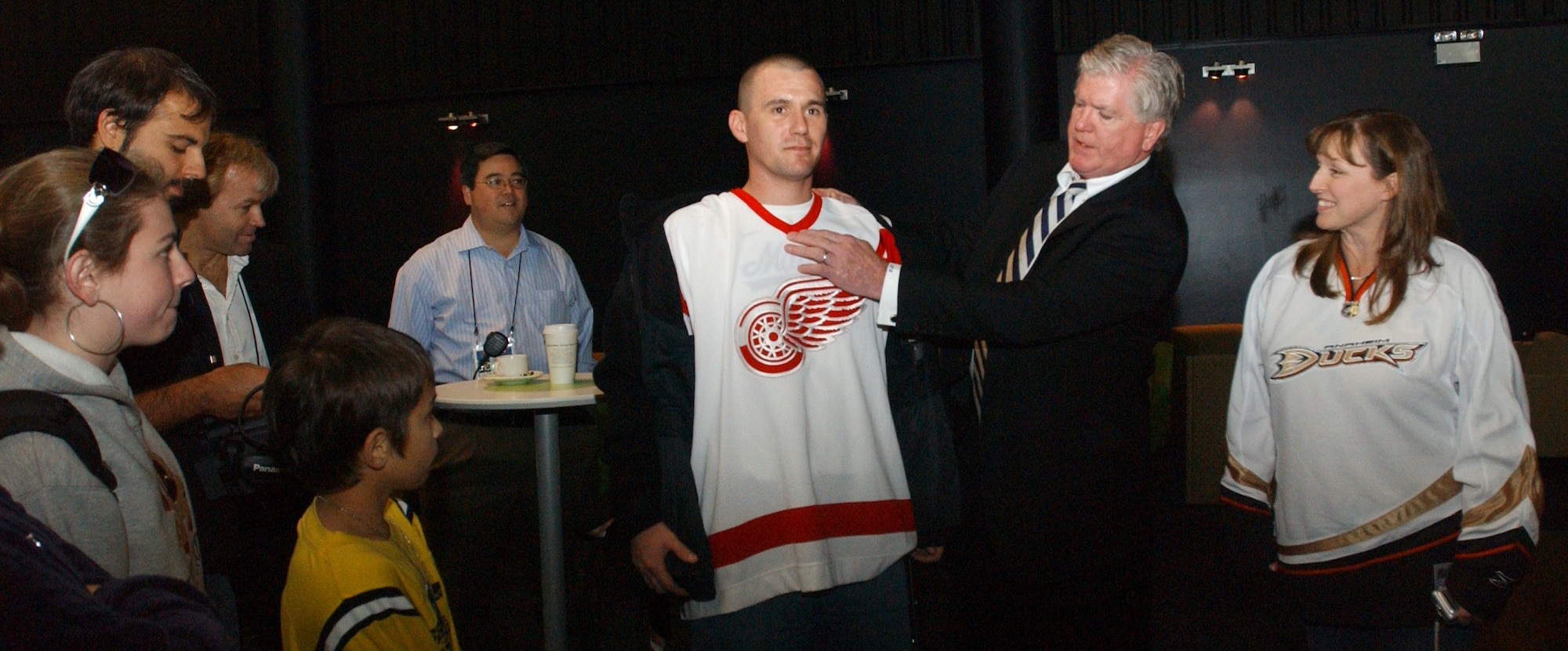 Brian Burke, general manager of Stanley Cup champions the Anaheim Mighty Ducks, explains the difference in heavyweight and a lightweight uniform using a Detroit Red Wings jersey with a little help from Staff Sgt. Steven Welch from 352nd Operations Support Squadron at the O2 Arena in London, Sept, 28, 2007. (U.S Air Force photo by Airman Brad Smith)                             
