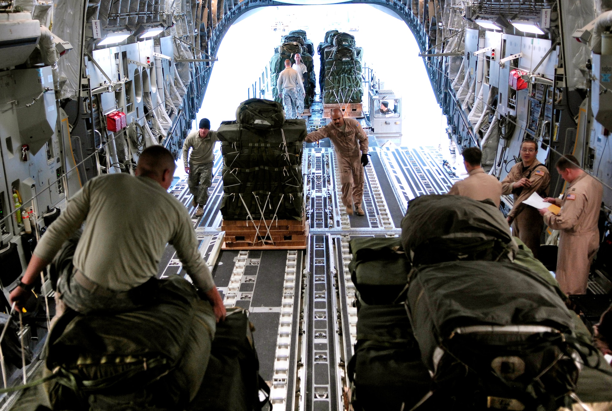 Army Spc. Joshua Black (left) attaches one of 62 parachute ripcords to the static line of a C-17 Globemaster III while crew members continue to load bundles Oct. 11 at Bagram Air Base, Afghanistan. The 62 cargo bundles were dropped from two C-17s to a drop zone in Afghanistan. This was the first time a combat cargo drop of this magnitude has taken place from two C-17s in formation over one drop zone. Specialist Black is a rigger with the 11th Quartermaster Company, 82nd Airborne. (U.S. Air Force photo/Staff Sgt. Brian Ferguson)
