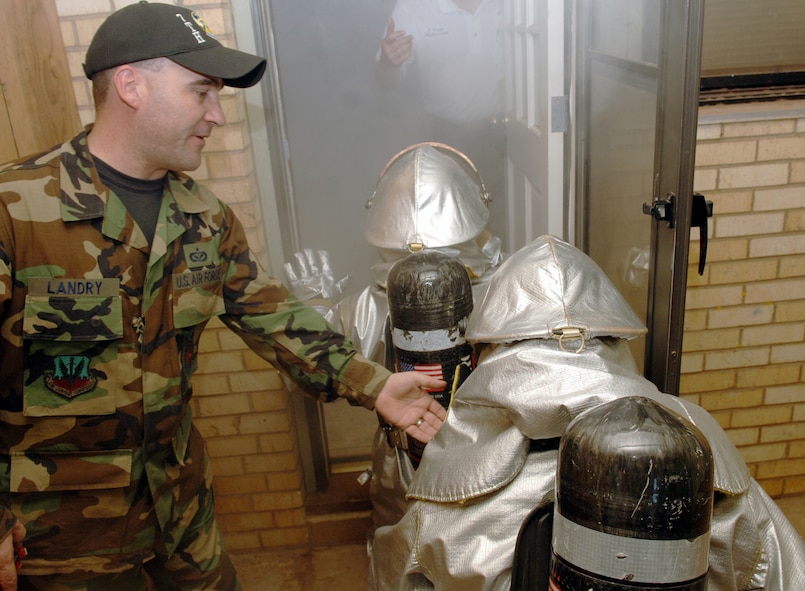 DYESS AIR FORCE BASE, Texas -- Tech. Sgt. Glenn Landry, 7th Civil Engineer Squadron firefighter, guides two Dyess servicemembers - a commander and an Airman - into a smoke-filled house Oct. 11 for the Commander's Challenge. The competition among 11 commanders and their troops was part of Fire Prevention Week events the fire department has been conducting since Oct. 7. (U.S. Air Force photo by Airman 1st Class Michael Breaux)
