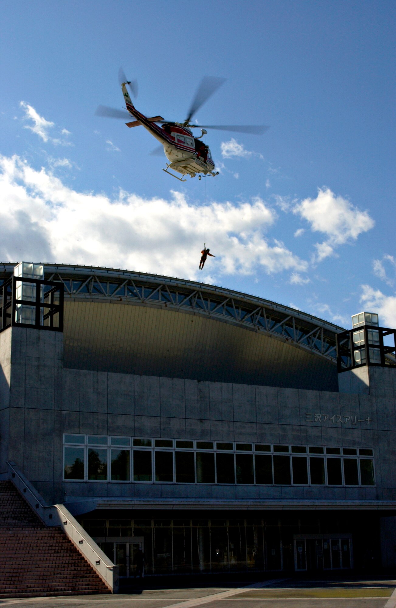 A helicopter from the Aomori Prefecture Disaster Preparedness Air Center lowers a rescue worker to retrieve a victim from the roof of the Misawa Ice Arena as part of the Misawa City Disaster Preparation Exercise Oct. 14 in Japan. The exercise involved personnel from Misawa City as well as Misawa Air Base. (U.S. Air Force photo/Airman 1st Class Eric Harris)
