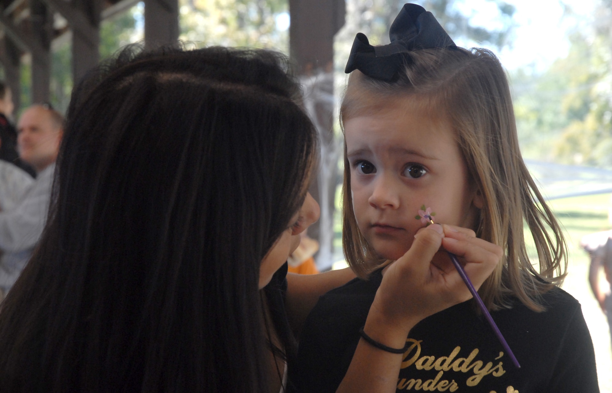 Zoe Benwitz, 3, daughter of Maj. Kyle Benwitz, gets a flower painted on her face by Christina Watkins, volunteer, during the 437th Operations Group Fall Fest at the base picnic grounds Saturday. Family members celebrated the new season with a variety of activities and contests. (U. S. Air Force photo/Airman Melissa White)