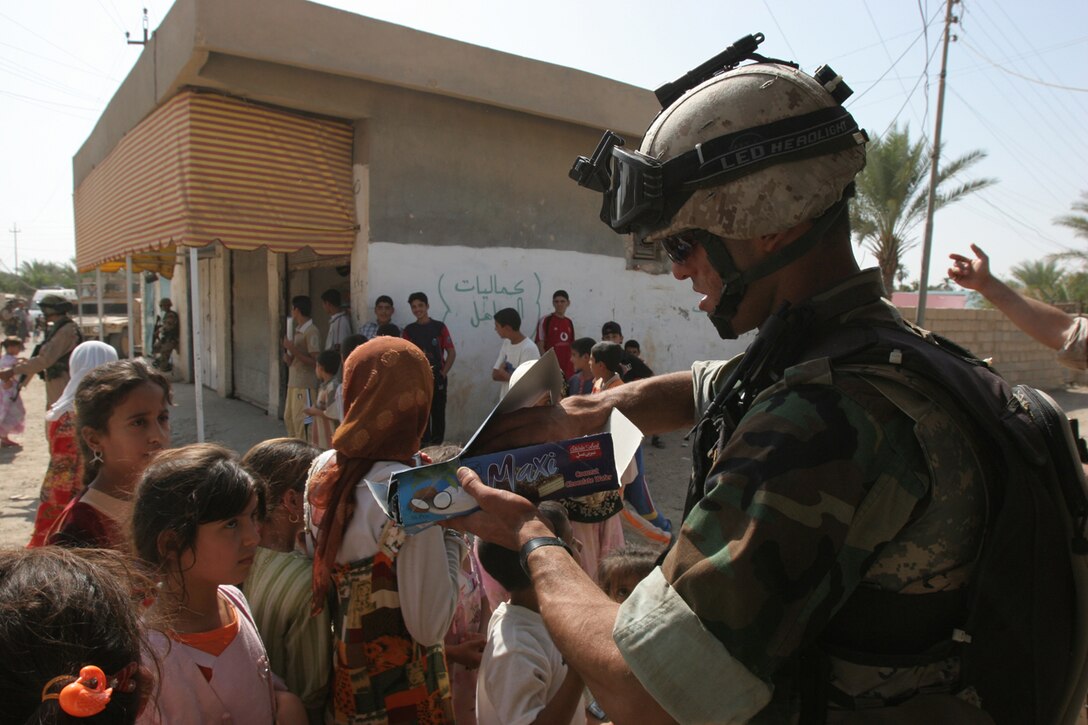 An Iraqi soldier with 1st Battalion, 3rd Brigade, 1st Iraqi Army Division, hands candy bars out to the children of Ghartan after a combined medical engagement held here Oct. 18.  The CME was held in a local school and surrounding the school were Iraqi soldiers standing security, searching and conducting vehicle checkpoints.  Female Marines with 2nd Marine Logistics Group politely searched females in a private shelter outside the school.  Corpsmen from Camp Al Taqaddum Surgical and Marines with the Military Transition Team helped provide and coordinate medical care for the local Iraqi population who were entering the school.