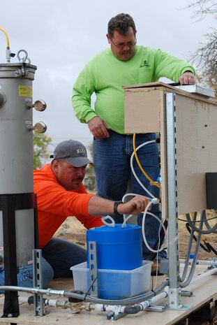 Kevin Roberts (left), CH2M HILL environmental technologist and Chris Goodrich (right), CH2M HILL remedial treatment systems construction manager, check the calibration of bleach injection pumps and collect data from pump controllers at a treatment skid at Site 31. (Photo by Airman 1st Class Robert Biermann)
