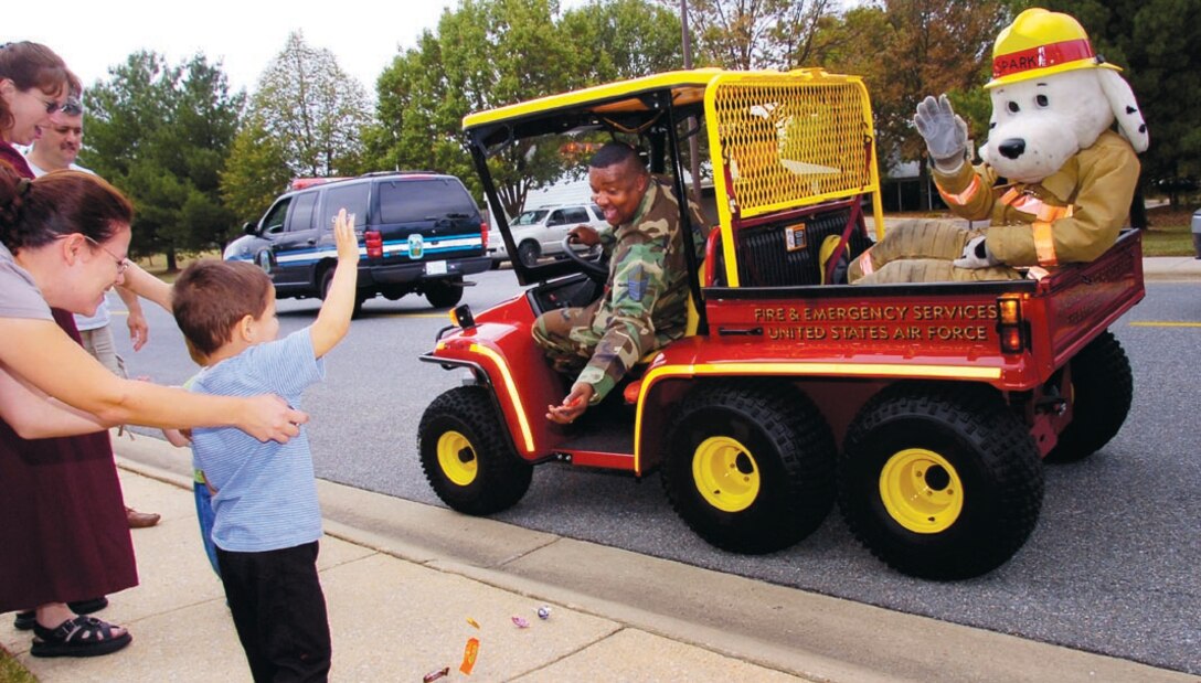 Madelyn Alvarez and her son, Miguel, 5, wave at Sparky the Fire Dog as Master Sgt. Timothy Knight tosses candy during the National Fire Prevention Week Kick-off Parade through base housing. Mrs. Alvarez is the wife of Special Agent Paul Alvarez, Headquarts Air Force Office of Special Investigations (US Air Force/Bobby Jones)