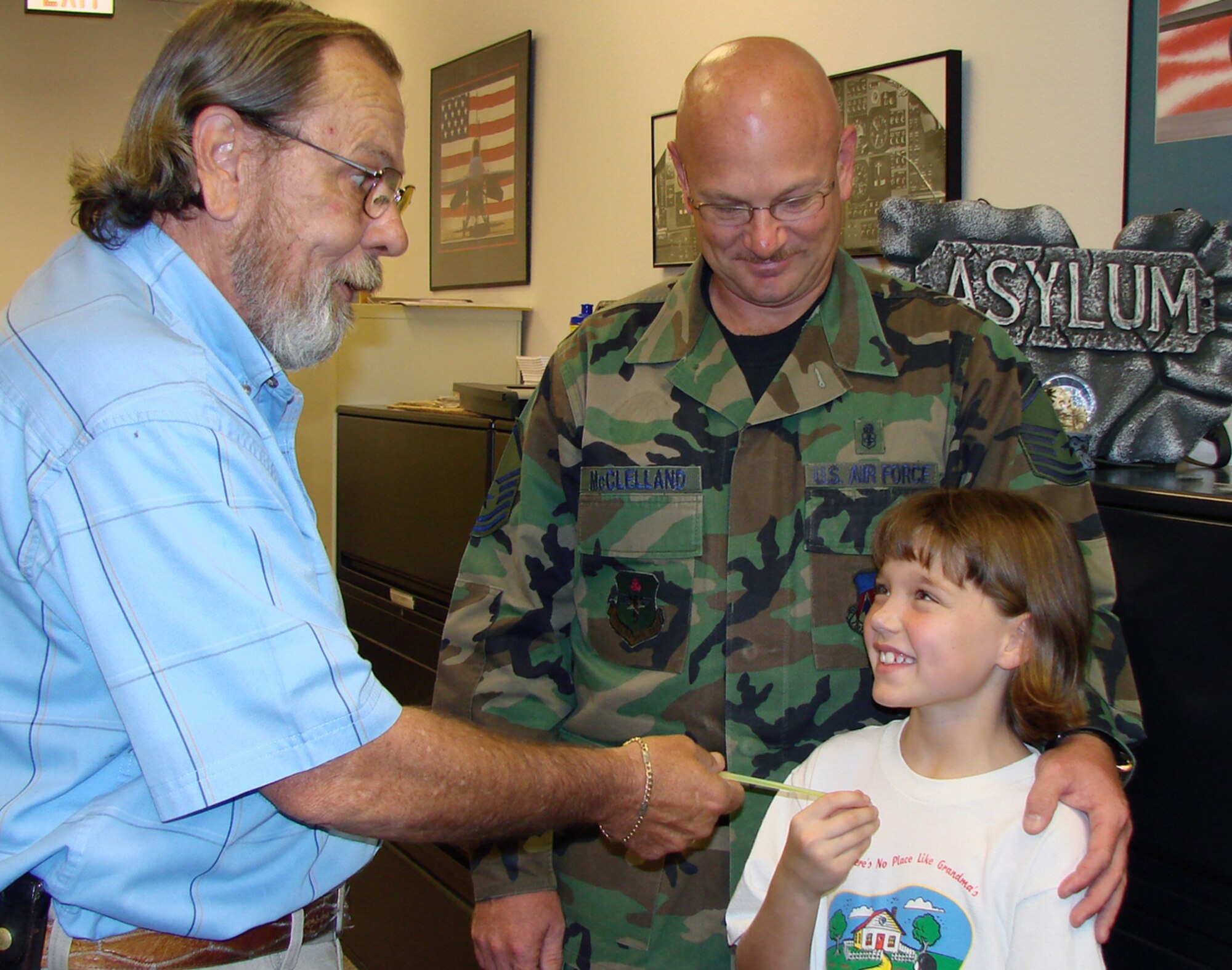 George Wagner, wing safety, gives a glow bracelet to 9-year-old Taylor McClelland while her father, Master Sgt. Dave McClelland, 71st Medical Support Squadron, looks on. Glow bracelets are available to children of military and Department of Defense civilian employees. Parents can pick up glow bracelets from the wing safety office from 7:30 a.m. to 4:30 p.m., Mondays through Fridays in Bldg. 455. (U.S. Air Force photo by Tech. Sgt. Mary Davis)