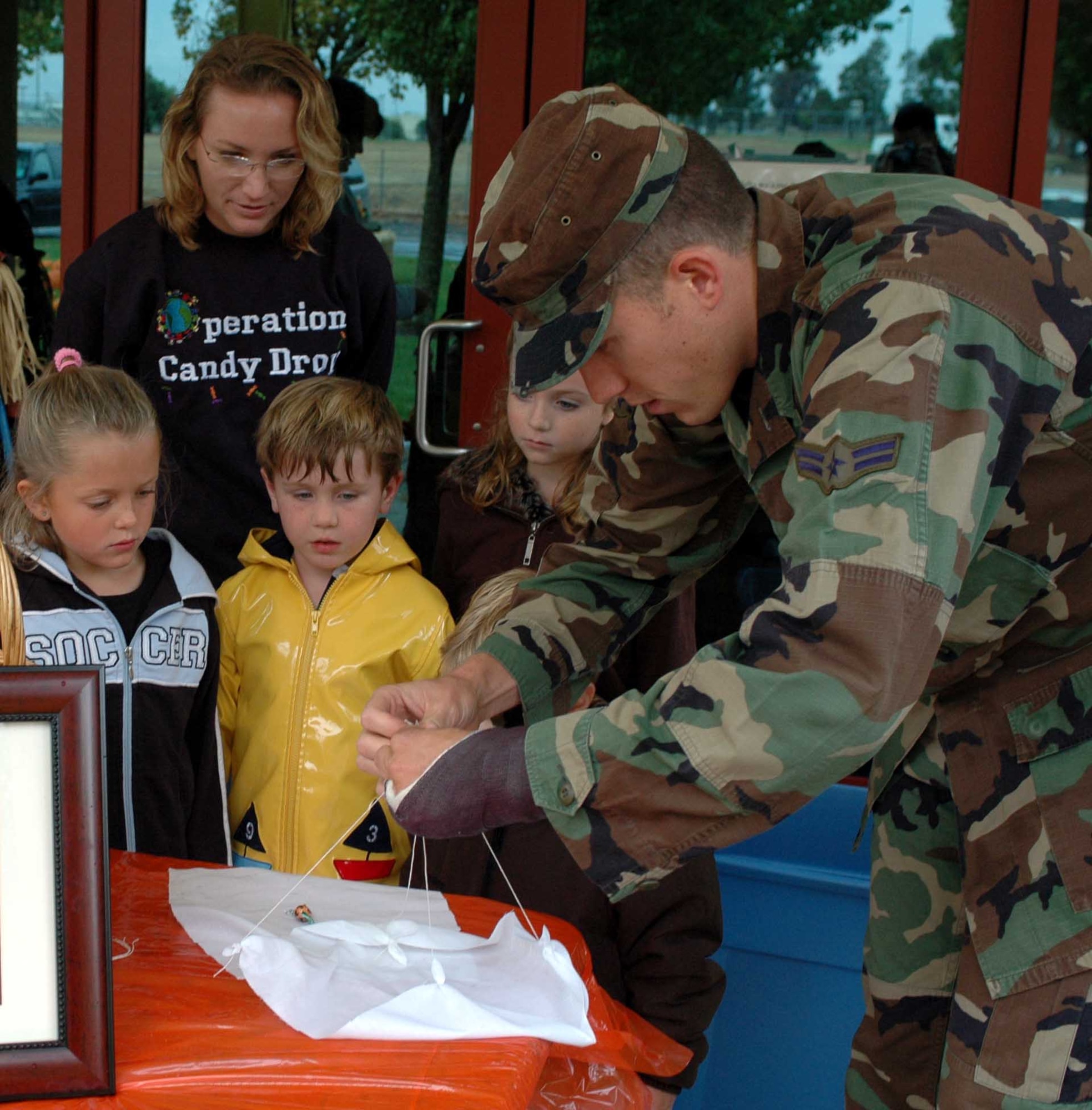 Airman 1st Class Ryan Williams, Operation Candy Drop volunteer, shows a group of children how to make a parachute that carries candy. Organizers of Operation Candy Drop, a drive to collect and deliver Halloween candy to Iraqi children, were inspired by the actions of 'The Candy Bomber,' Col. Gail Halvorsen, (retired), a Berlin Airlift pilot who delivered candy to children via parachute at the end of World War II. (U.S. Air Force photo/Staff Sgt. Matthew McGovern)