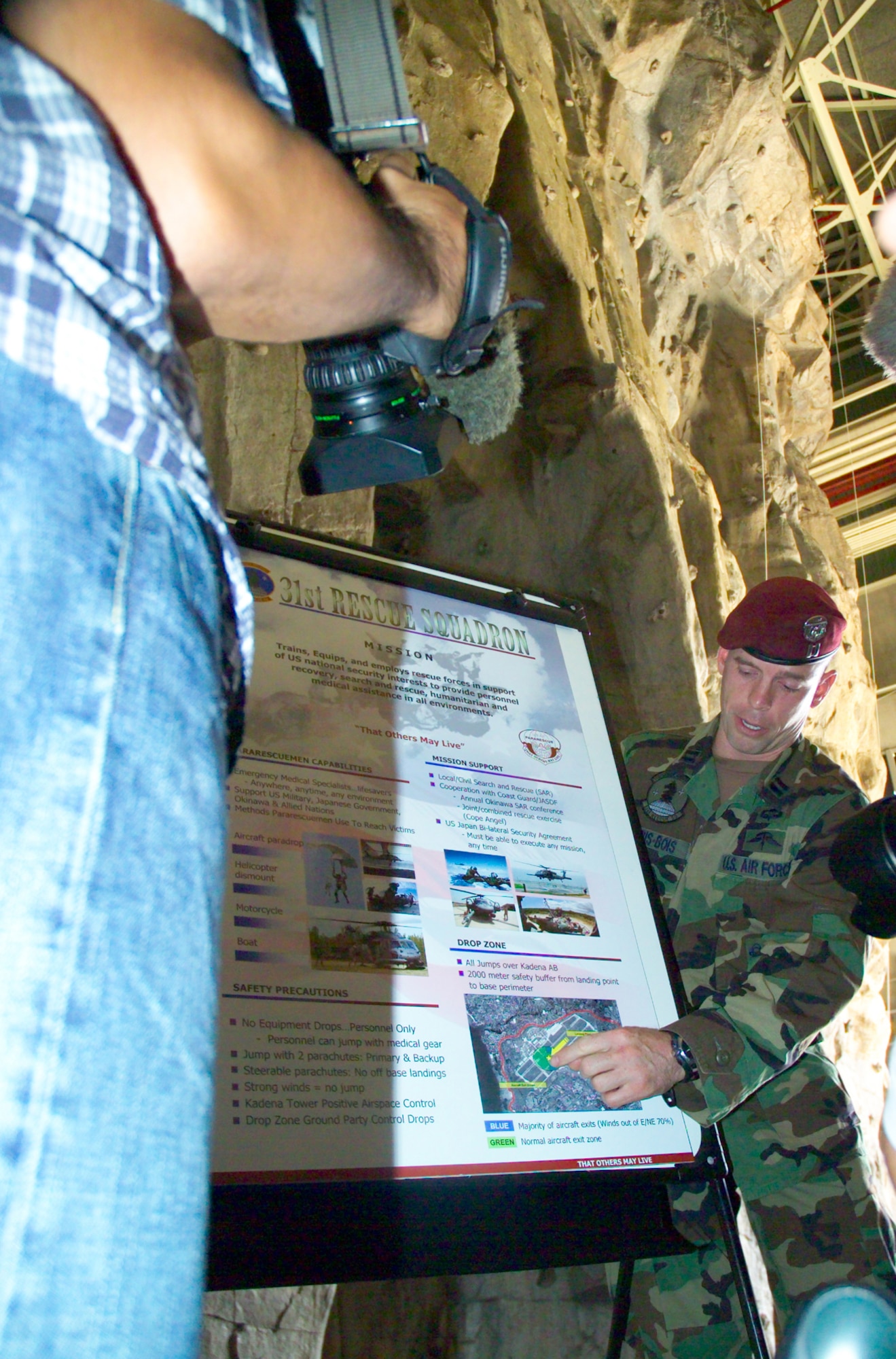 A member of the 31st Rescue Squadron explains to members of the Japanese media capabilities of pararescuemen before a proficiency paradrop on Kadena’s airfield Oct. 19. More than 20 members of the media attended the briefing about the airborne operation and observed the drop.  (courtesy photo/Scott Hallford)