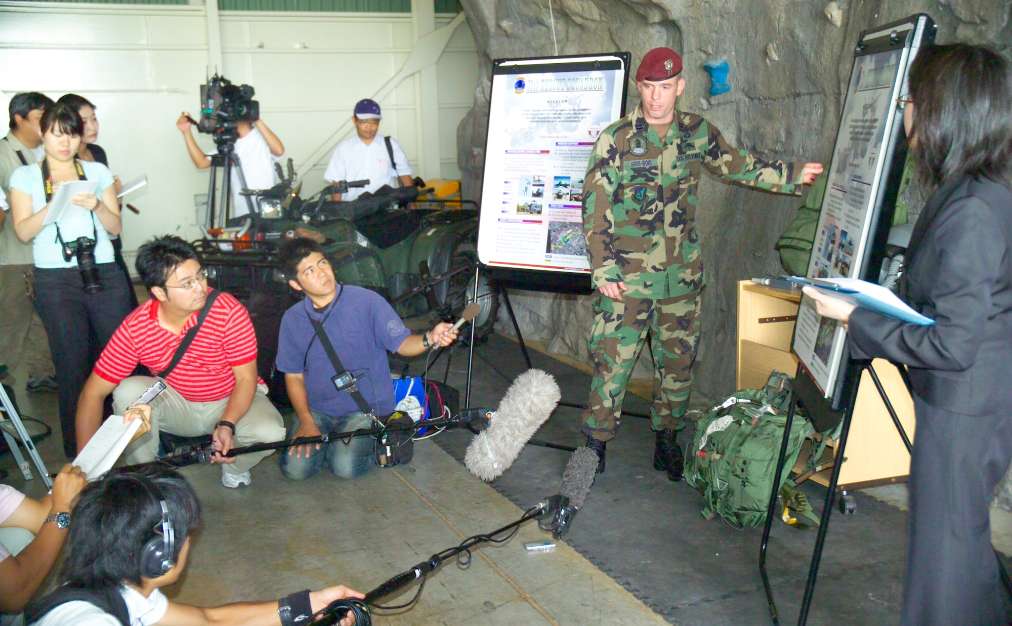 A member of the 31st Rescue Squadron explains to members of the Japanese media capabilities of pararescuemen before a proficiency paradrop on Kadena’s airfield Oct. 19. More than 20 members of the media attended the briefing about the airborne operation and observed the drop. (courtesy photo/Scott Hallford)