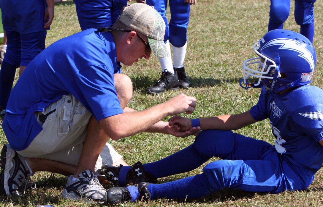 First Lt. David R. McGrath applies wrist tape to a player on the Jacksonville Storm just minutes before the start of their game against the New Bern Knights at commons field Oct. 20.  McGrath has coached the team during his off-time for the past two years, bringing the team to a record of 13 wins.  The team is scheduled to take on the Greenville Titans Nov. 3, a game that could land them a seat in the Pop Warner Championship.