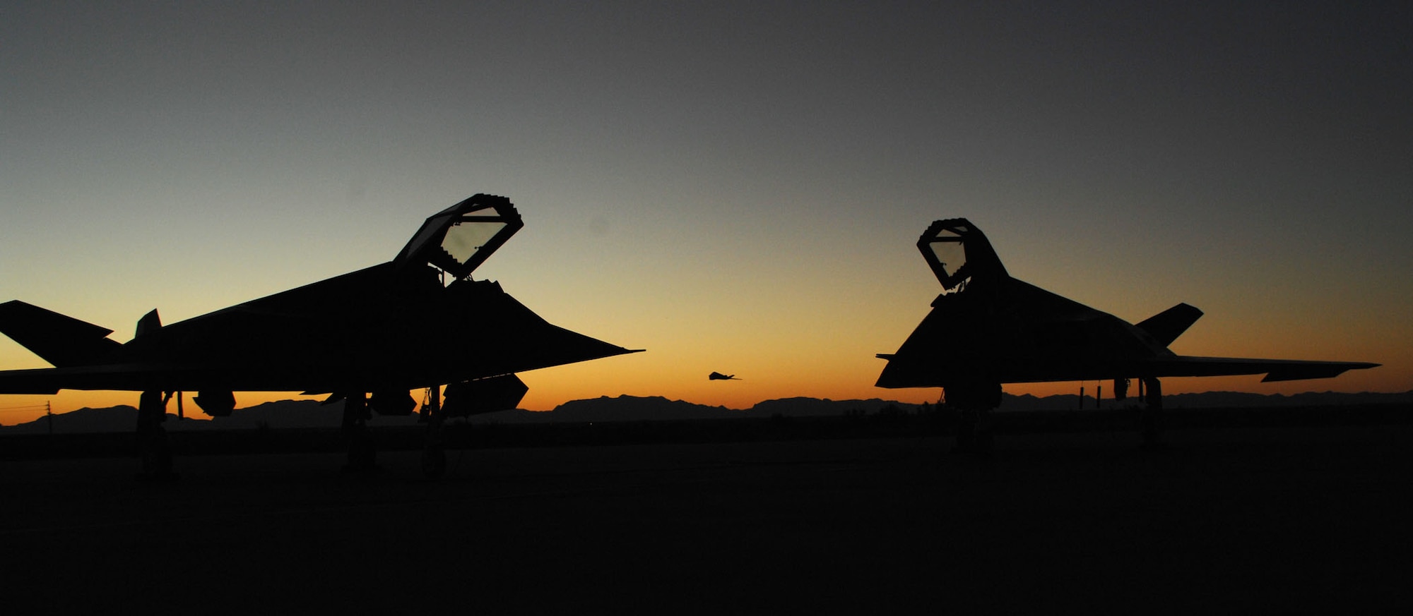 Two F-117A Nighthawk sit on the Holloman flightline as another F-117A takes off into the sunset. (U.S. Air Force photo/ Airman 1st Class Heather Stanton)