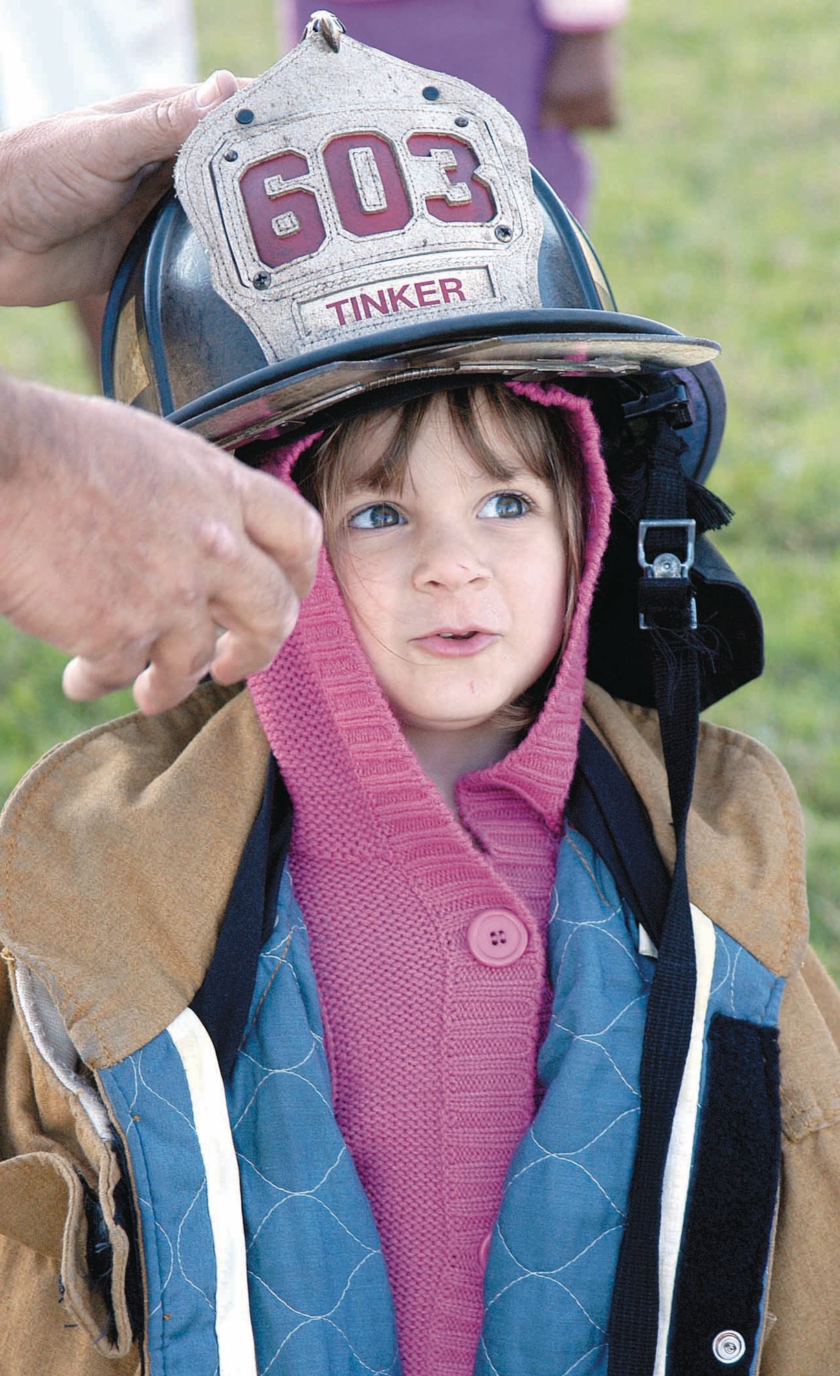 Big hands steady a big helmet on Victoria Meiss's small frame during a Fire Prevention Week visit by firefighters to the Child Development Center East. Kids lined up to try on the adult-sized protective gear and to sit in the dirver's seat of a big, red fire truck. (Air Force photo by Margo Wright)
