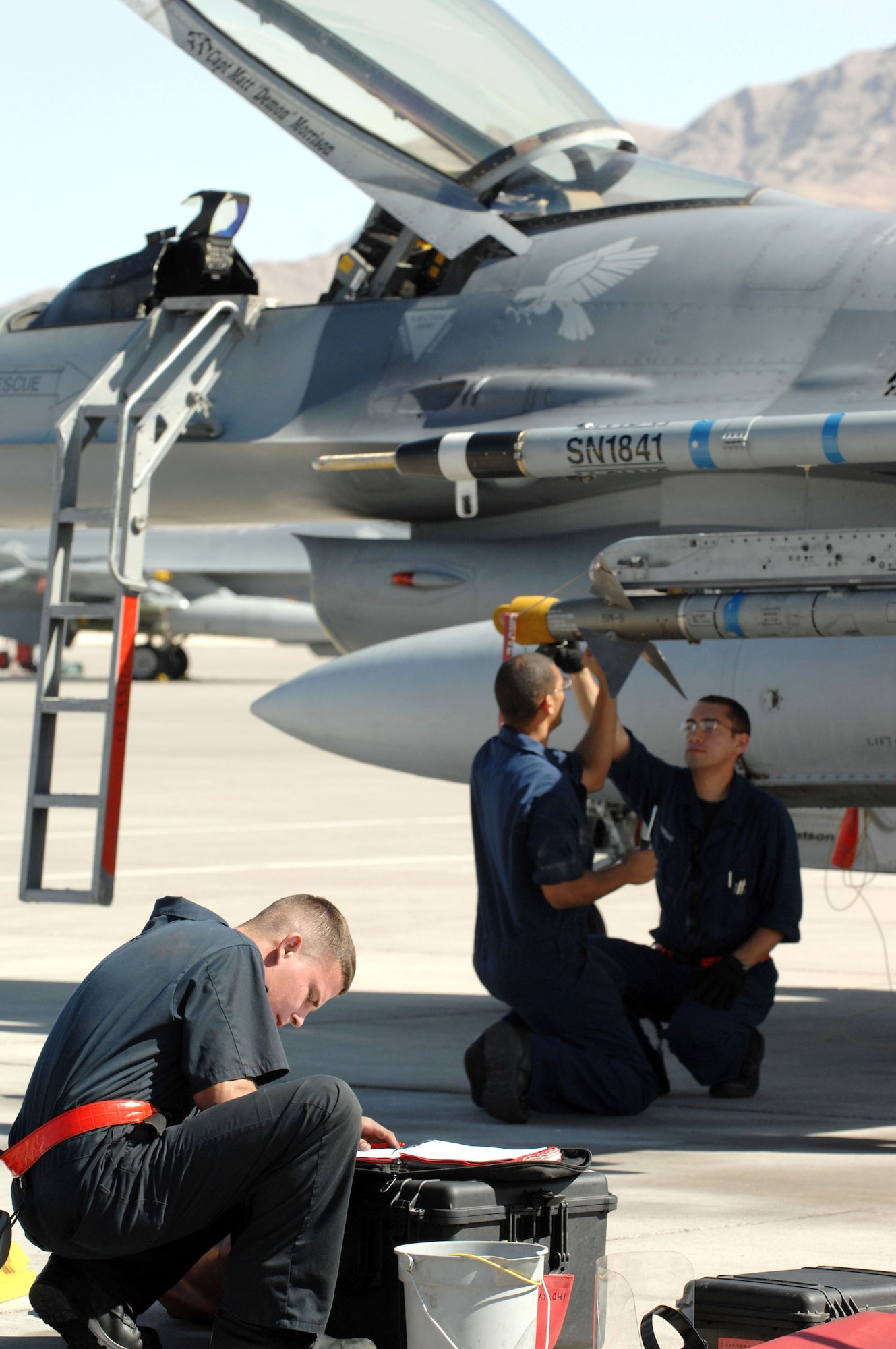 Senior Airman Michael Blankenship (left) fills out F-16 Fighting Falcon post flight forms while Senior Airmen Gabriel Sheppard and Curtis Morgan change an argon bottle on an AIM-9 missile Oct. 18 at Nellis Air Force Base, Nev. The three Airmen are crew chiefs assigned to the 63rd Fighter Squadron from Luke AFB, Ariz. The 63rd FS is at Nellis AFB supporting the F-15 Eagle Weapons School Instructor Course in an adversary tactics role. (U.S. Air Force photo/Master Sgt. Kevin J. Gruenwald)
