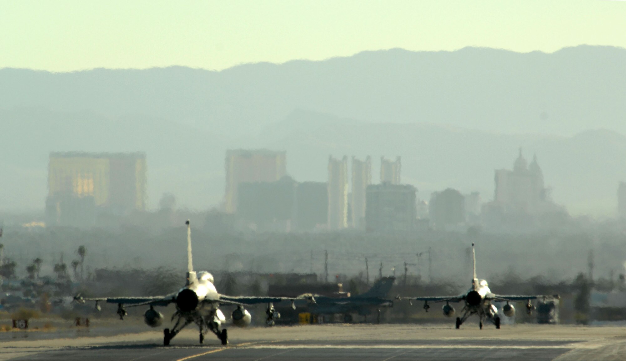 With Las Vegas as a backdrop, two F-16 Fighting Falcons taxi out Oct. 18 at Nellis Air Force Base, Nev. The F-16s are assigned to the 63rd Fighter Squadron from Luke AFB, Ariz. The 63rd FS is at Nellis AFB supporting the F-15 Eagle Weapons School Instructor Course in an adversary tactics role. (U.S. Air Force photo/Master Sgt. Kevin J. Gruenwald) 
