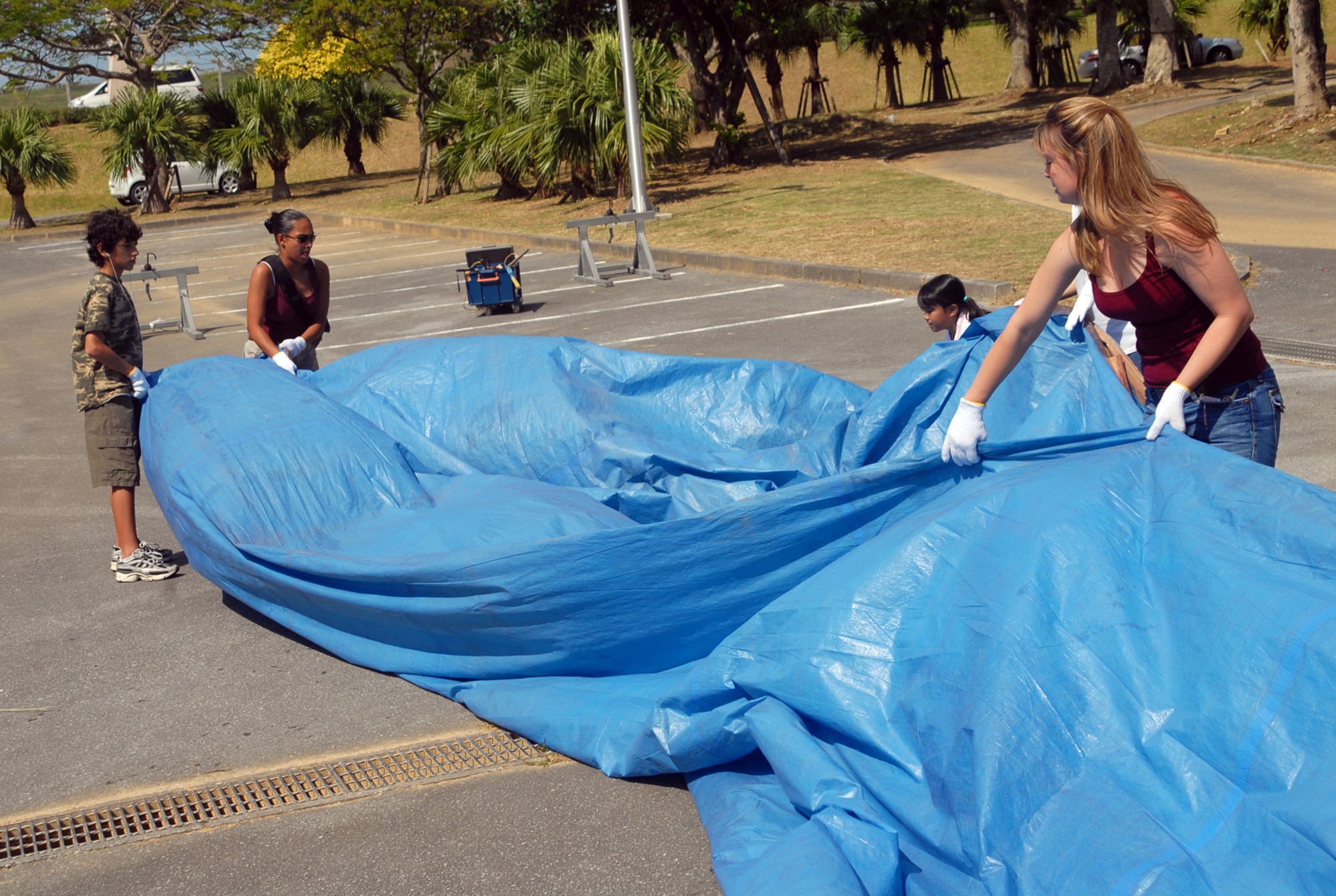Team Kadena members  work together to remove the tarps covering large sections of rope Oct. 20.  The members are volunteers who participated in making a 100 meter long rope to be used for a tug-of-war at the upcoming Okinawa City International Carnival. (U.S. Air Force photo/Staff Sgt. Christopher A. Marasky)