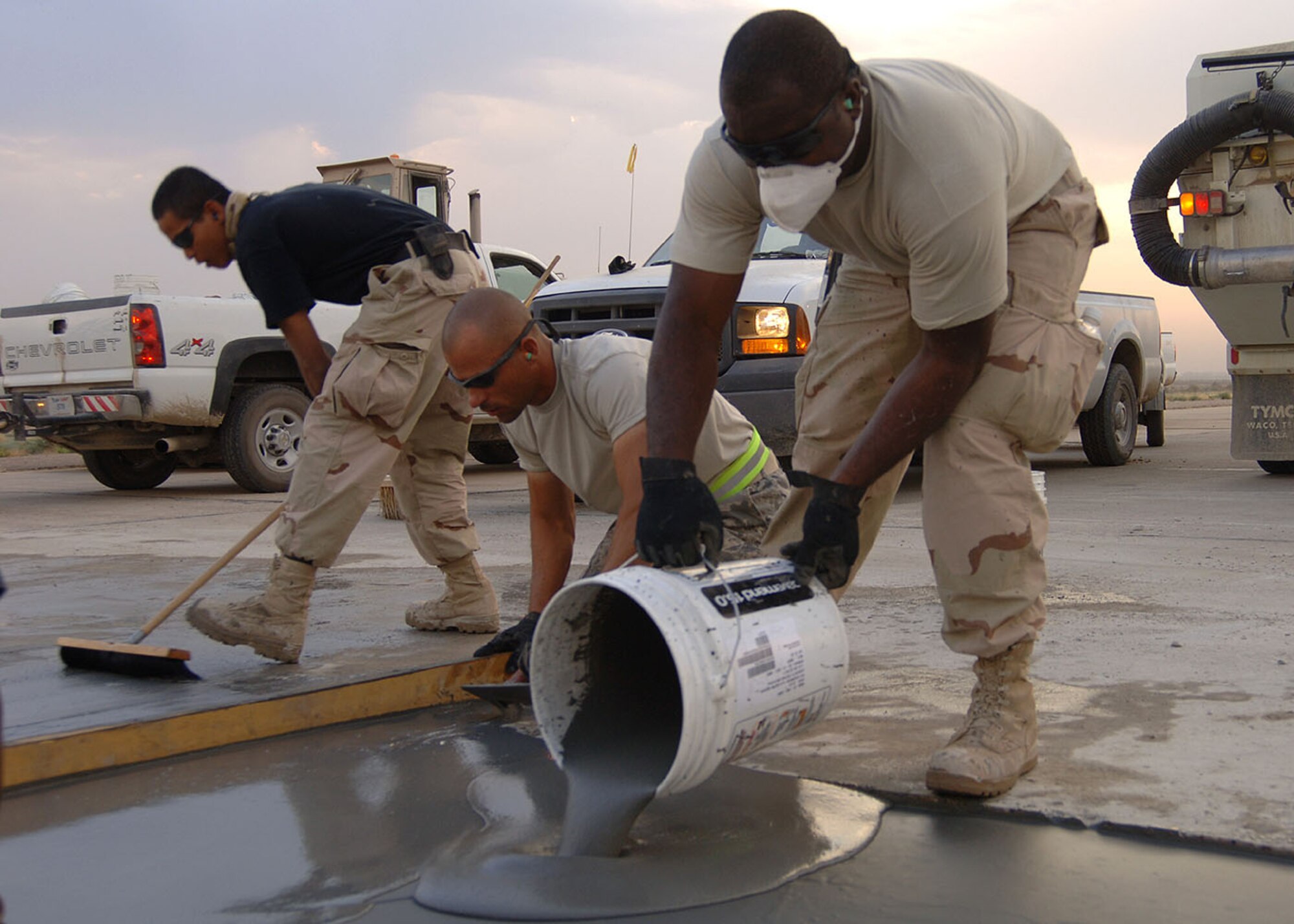 SATHER AIR BASE, Iraq -- Tech. Sgt. Freddie Garrette pours freshly mixed concrete into a 100 square foot spall repair area Oct. 6 while Tech. Sgt. Jeff Jones, center, smoothes the edges and Senior Airman Wilson Quinante brushes the surface of a smoothed section to give it an anti-skid surface. The 447th Expeditionary Civil Engineer Squadron Heavy Equipment Operations “Dirt Boys” repair damaged surface areas on the airfield here each Saturday morning. The team gets an early start, often working before sunrise, to beat the daytime high temperatures, which helps ensure a proper mixture cure time and a stronger slab. The team must also work quickly to limit the amount of time airfield operations are affected while repairs are done. Sather AB is the busiest airfield in Iraq, averaging 4,000 transient aircraft activities each month. Sergeant Garrette is deployed from the Tennessee Air National Guard. Sergeant Jones is deployed from Elmendorf Air Force Base, Alaska.  Airman Quinante is deployed from Eglin Air Force Base, Fla. (Staff Sgt. Jennifer Lindsey)
