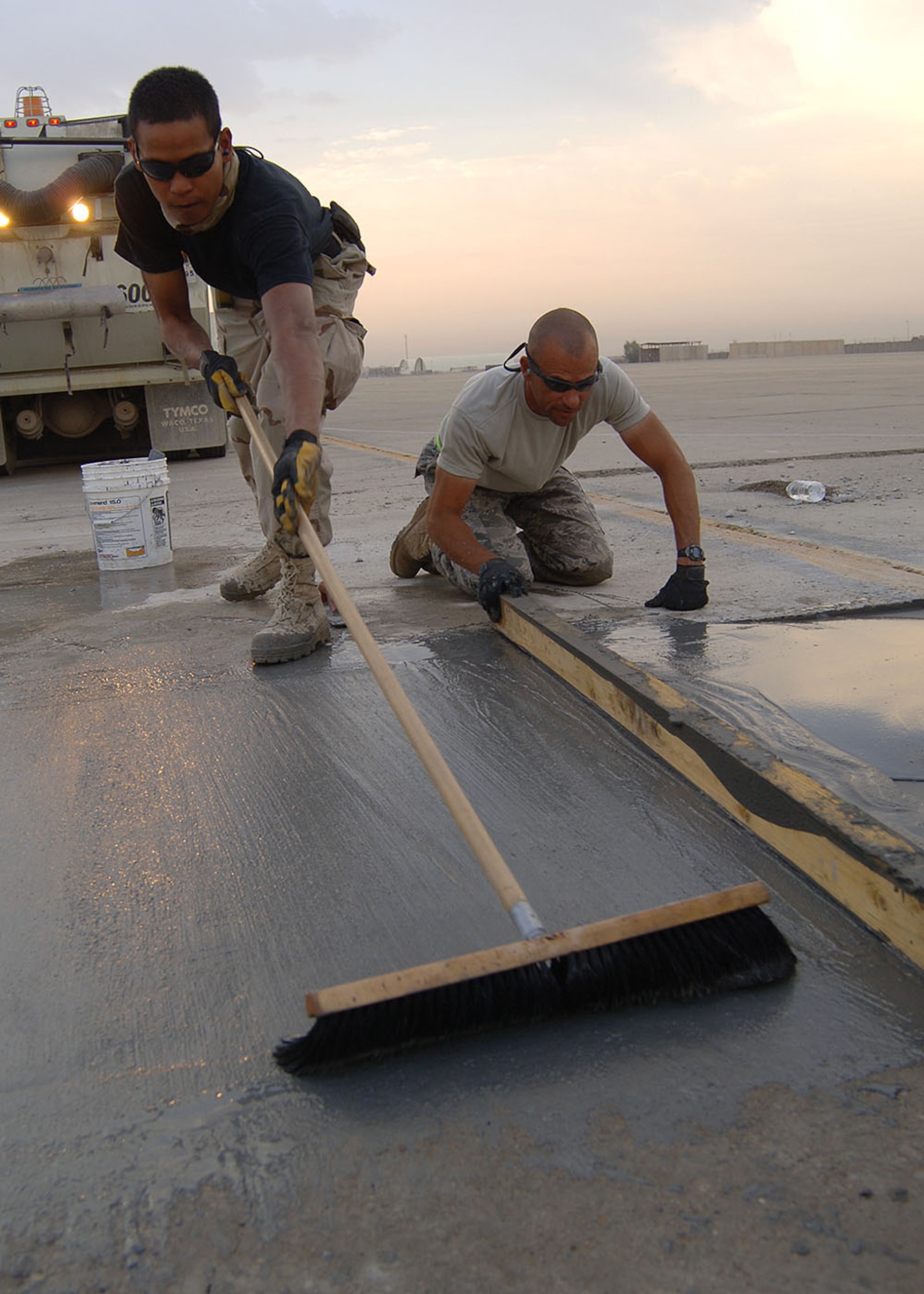 SATHER AIR BASE, Iraq -- Senior Airman Wilson Quinante brushes over newly poured concrete to even out the surface and give it a rough finish for anti-skid purposes, as Tech. Sgt. Jeff Jones uses a 2-by-4-inch board as a scree to push forward and smooth the mixture in the ramp area for repair. The 447th Expeditionary Civil Engineer Squadron Heavy Equipment Operations “Dirt Boys” repair damaged surface areas on the airfield here each Saturday morning. The team gets an early start, often working before sunrise, to beat the daytime high temperatures, which helps ensure a proper mixture cure time and a stronger slab. The team must also work quickly to limit the amount of time airfield operations are affected while repairs are done. Sather AB is the busiest airfield in Iraq, averaging 4,000 transient aircraft activities each month. Airman Quinante is deployed from Eglin Air Force Base, Fla. (Staff Sgt. Jennifer Lindsey)
