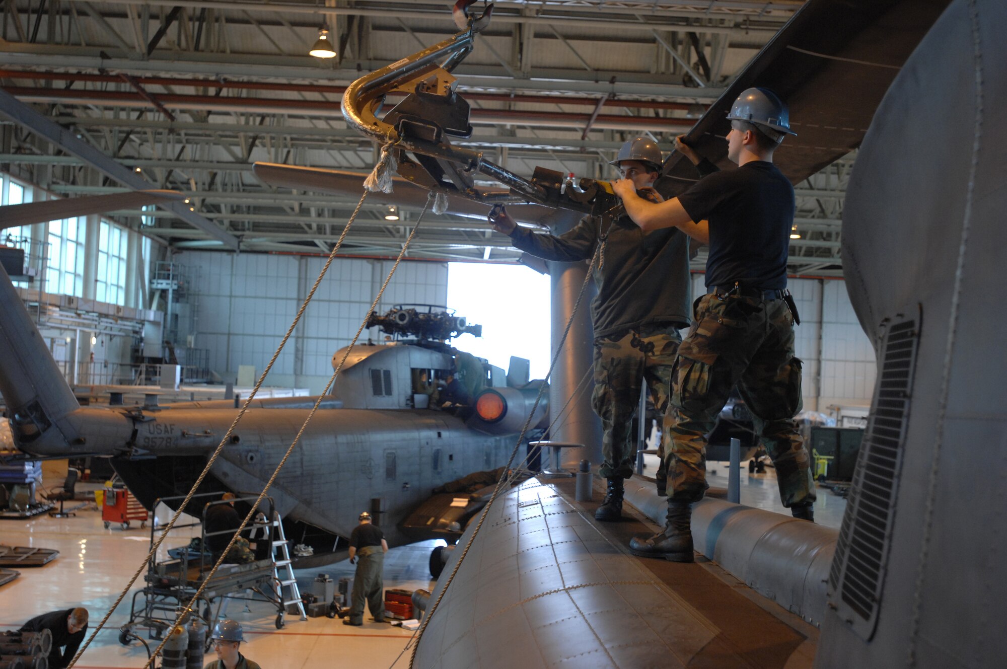Airman 1st Class Chris Ollivier, a crew chief, and hydraulics specialist, Airman 1st Class Lyle McFarlan, both in the 352nd Maintenance Squadron guide the overhead hoist under one of six rotor blades on an MH-53M Pave Low IV Helicopter assigned to the 21st Special Operations Squadron, Oct. 02, 2007, RAF Mildenhall, England. The hoist will gently lift each blade to remove tension before the eight bolts that hold it in-place can be removed. Once the tear down process is complete, it usually takes an average two days; the helicopters will be transported to the Aerospace Maintenance and Regeneration Group in Tucson, Ariz., commonly known as the 'Boneyard.' All Pave Low helicopters in the Air Force inventory are due to be grounded by October 2008. (U.S. Air Force photo by Tech. Sgt. Tracy L. DeMarco)
