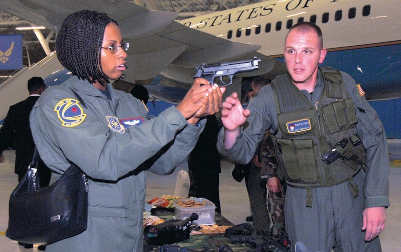 Tech. Sgt. Joey Kimbrough, 316th Security Forces Squadron Raven, explains the operation of a 9mm weapon to Staff Sgt. Cheneldrea Moore, 1st Helicopter Squadron, during a hands-on demonstration during the Ravens security demonstration inside hangar four on Sept. 25. The Raven Team's mission is to provide security for all special air missions carrying the President, Vice President and other senior government leaders during their official travel. (US Air Force/SSgt Suzanne Day)