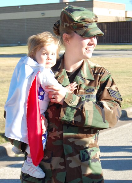 Staff Sgt. XXXX carries XXX who is dressed as "Evel Knievel," her favorite character from the stories read during October's Literacy Month celebration.  Throughout the month, the children listened to stories and were then asked to come dressed as their favorite character for a parade.  Costumes ranged from dinosaurs to princesses and other creative outfits.   (U.S. Air Force photo/2nd Lt. Megan Togni) 
