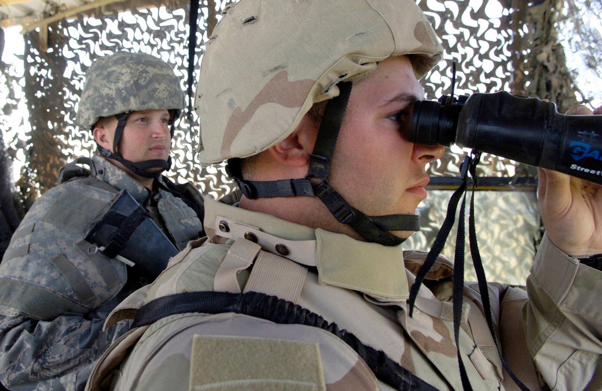 Airman 1st Class Micheal Ramsey, 332nd Expeditionary Security Forces Squadron watchtower sentry, scans the north perimeter of the base here for suspicious activity while sentry Staff Sgt. Robert Meade stands at the ready postition. Sergeant Meade is from Lackland Air Force Base, Texas and Airman Ramsey is from Vandenberg AFB, Calif. (U.S. Air Force photo/Senior Airman Travis Edwards)