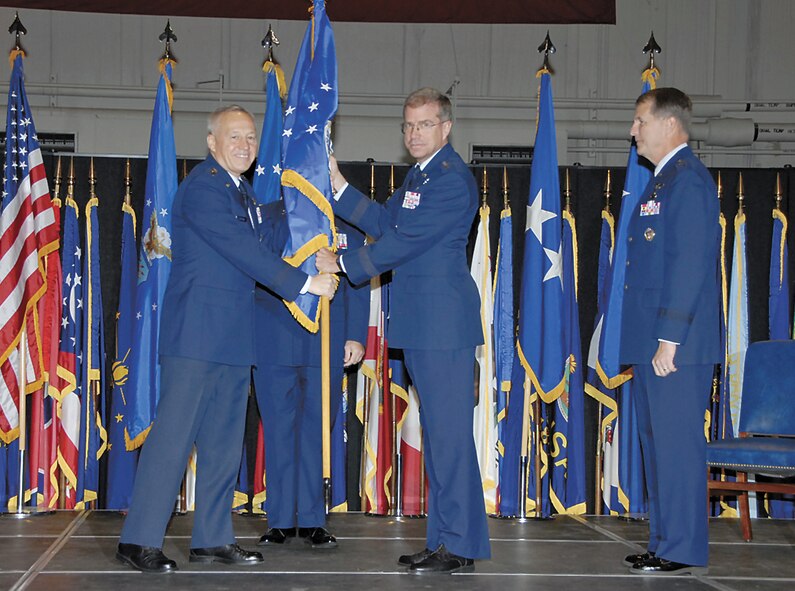 Gen. Bruce Carlson passes the AFRL flag to Maj. Gen. Curtis Bedke as he assumes command of the Air Force Research Laboratory at Wright-Patterson Air Force Base. Outgoing commander Maj. Gen. Ted Bowlds looks on. Bowlds, a Lt. Gen. select, will next command Electronic Systems Center at Hanscom Air Force Base, Mass. (Christy Webb/Skywrighter photo) 