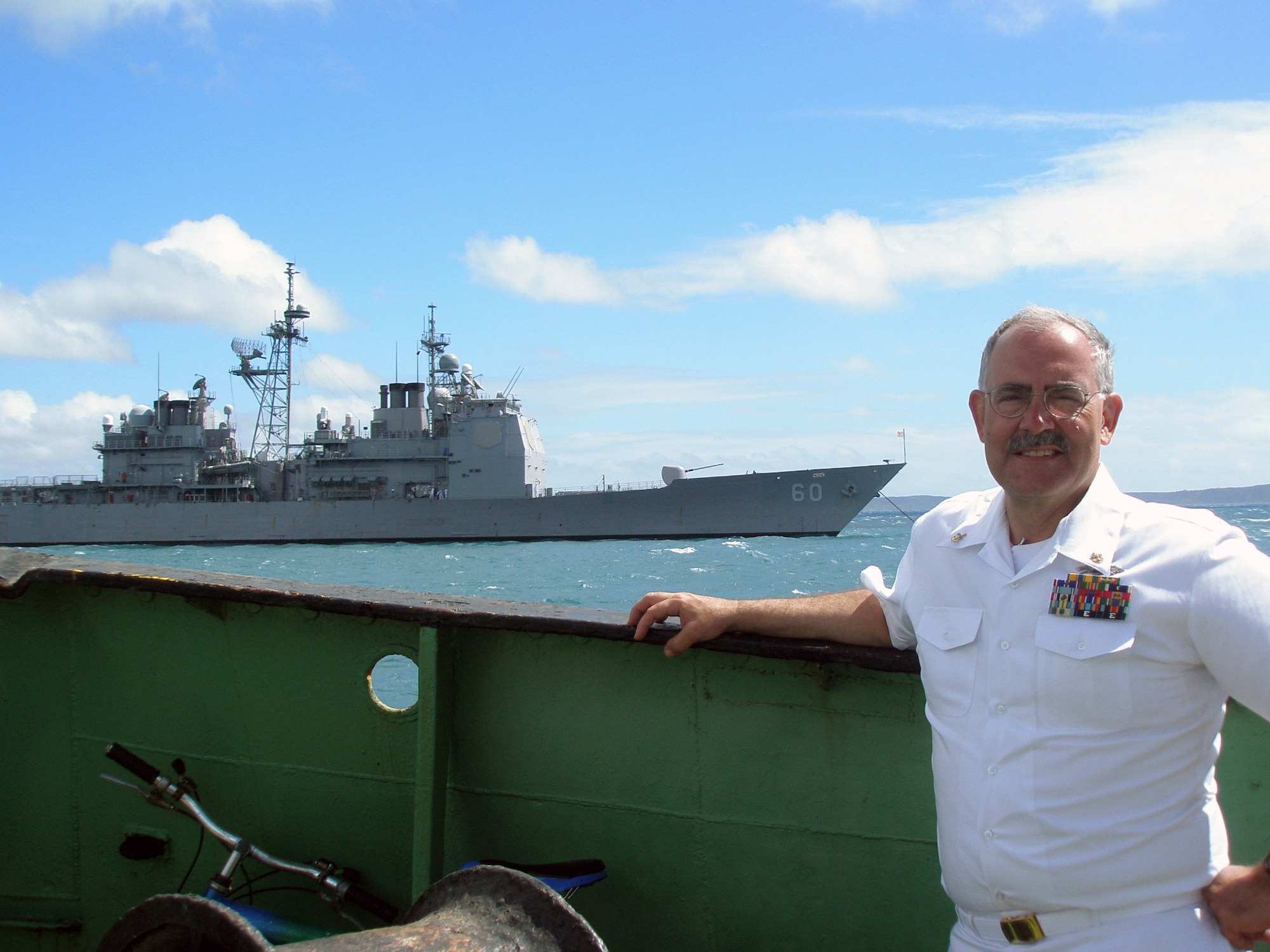 Navy Chief Petty Officer Robert Orton stands aboard a Malagasy naval tug boat as the USS Normandy, a U.S. Navy guided missile cruiser, anchors in off shore. Chief Orton, a Navy reservist and personnel technician at the Air Reserve Personnel Center, recently deployed to Madagascar as part of the Navy's Maritime Partnership Program. (Courtesy photo)