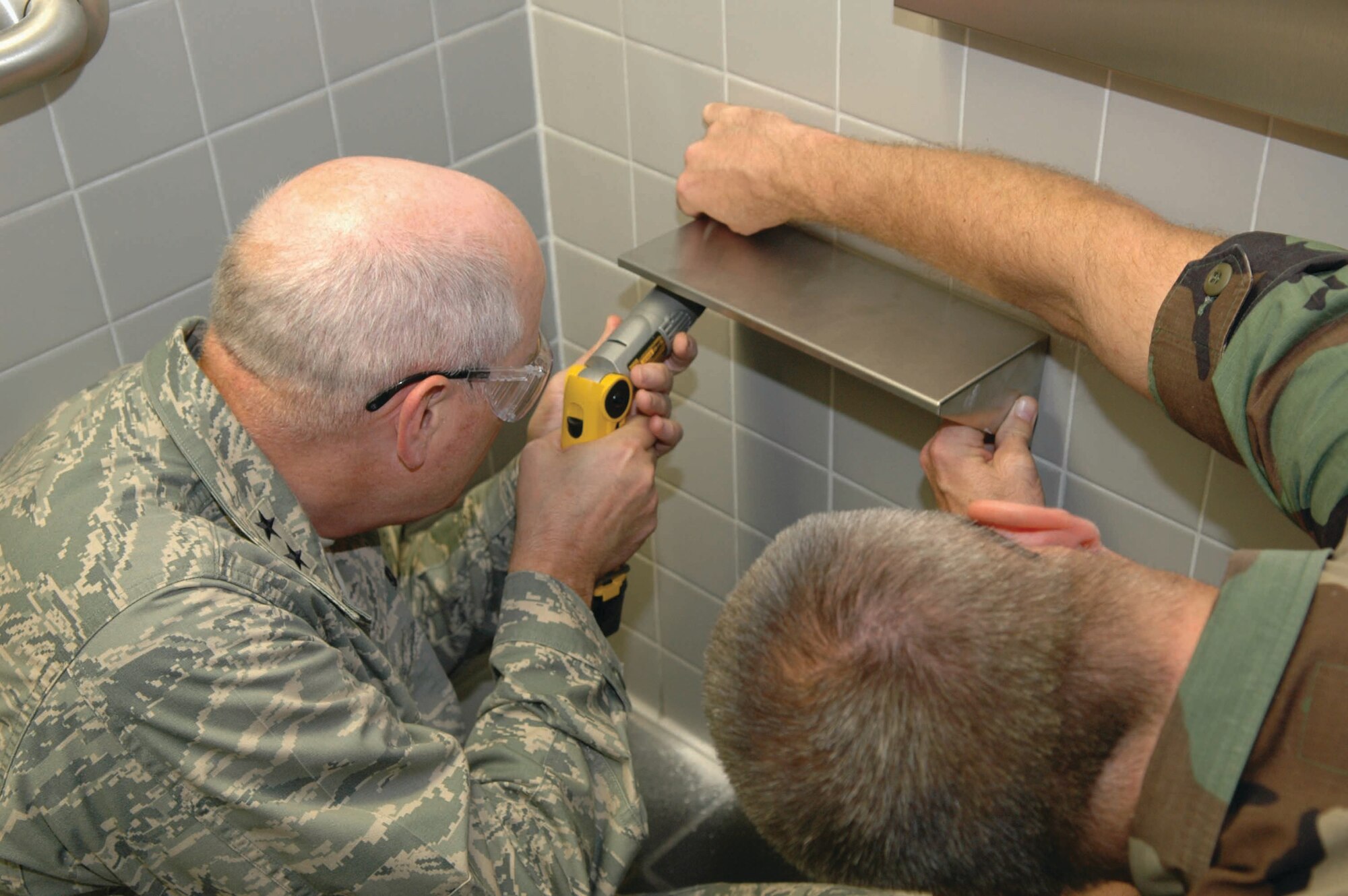 Capt Jeff Zdenek, a career broadening officer, holds a handicap bathroom stall door steady as Maj. Gen. Loren Reno, Oklahoma City Air Logistics Center commander, attaches a handle to make it easier for special needs workers to use the restroom. (Air Force photo by Ron Mullan)