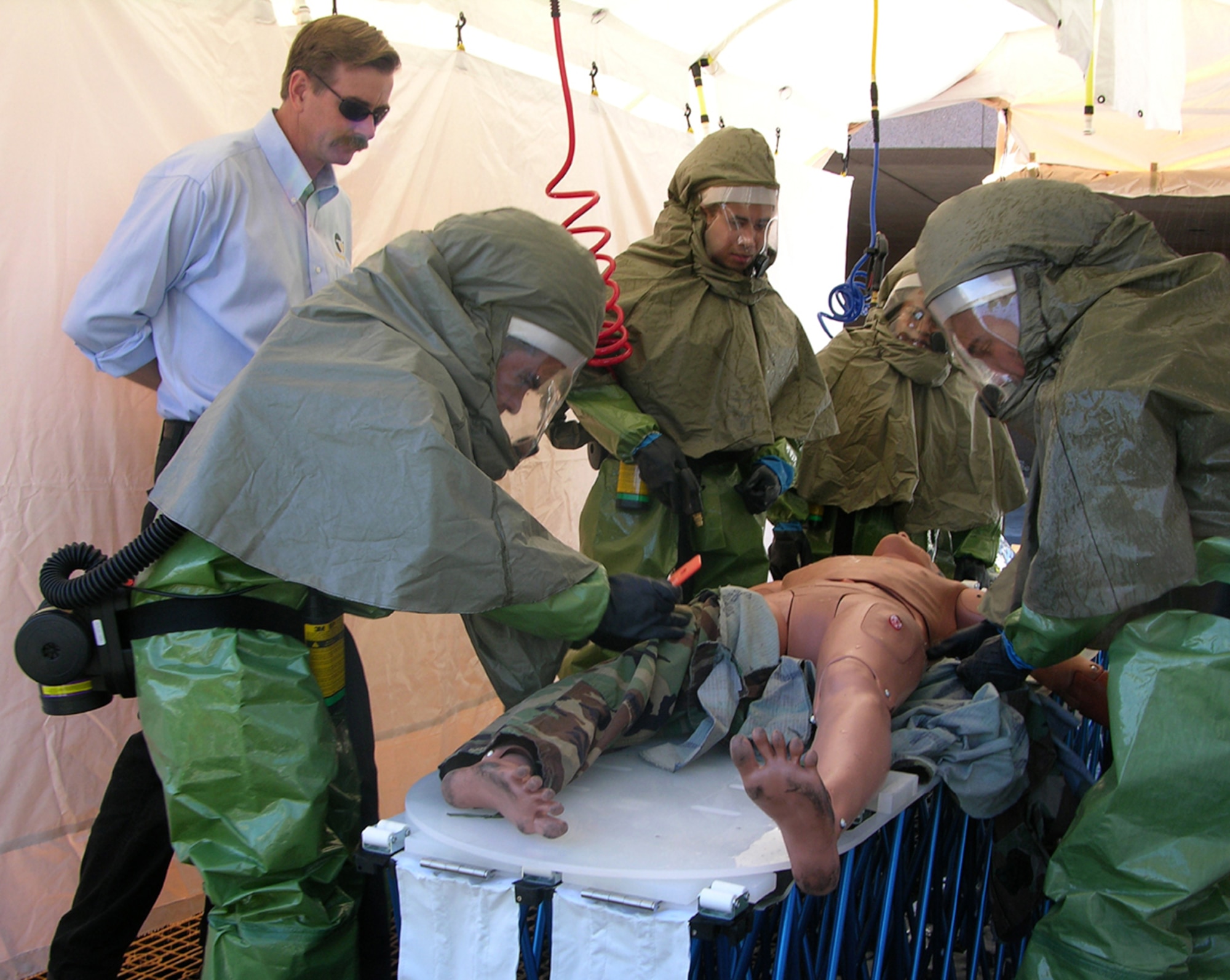 Tom Bocek, (far left) a training representative with Air Combat Command, teaches decontamination procedures to Airmen from a 99th Medical Group In-Place Patient Decontamination team outside the Mike O'Callaghan Hospital here, Oct. 25. The three days of training scenarios were aimed at teaching Airmen how to protect medical facility resources and treat patients after a chemical, biological, radiological, nuclear or explosive attack. (U.S. Air Force photo by Tech. Sgt. Benjamin Reynoso)