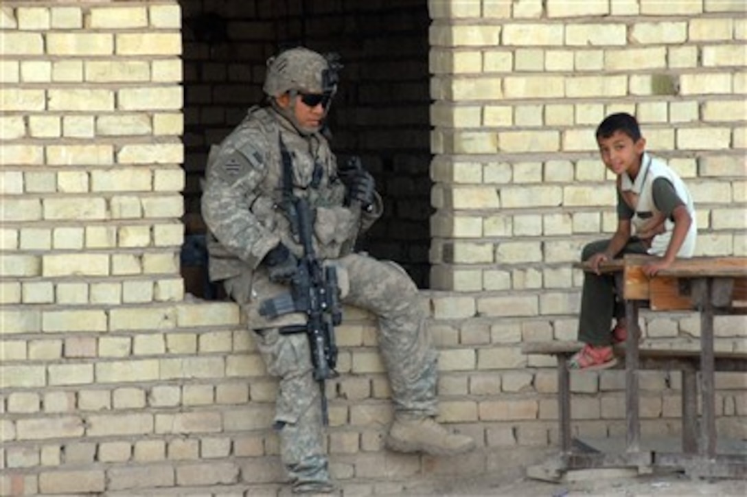 A U.S. Army soldier provides security while he talks to an Iraqi boy during a humanitarian mission at the Haifa School in Arab Jabour, Iraq, on Oct. 15, 2007.  The mission is being accomplished by soldiers assigned to Headquarters and Headquarters Company, 1st Battalion, 30th Infantry Regiment, 3rd Infantry Division.  