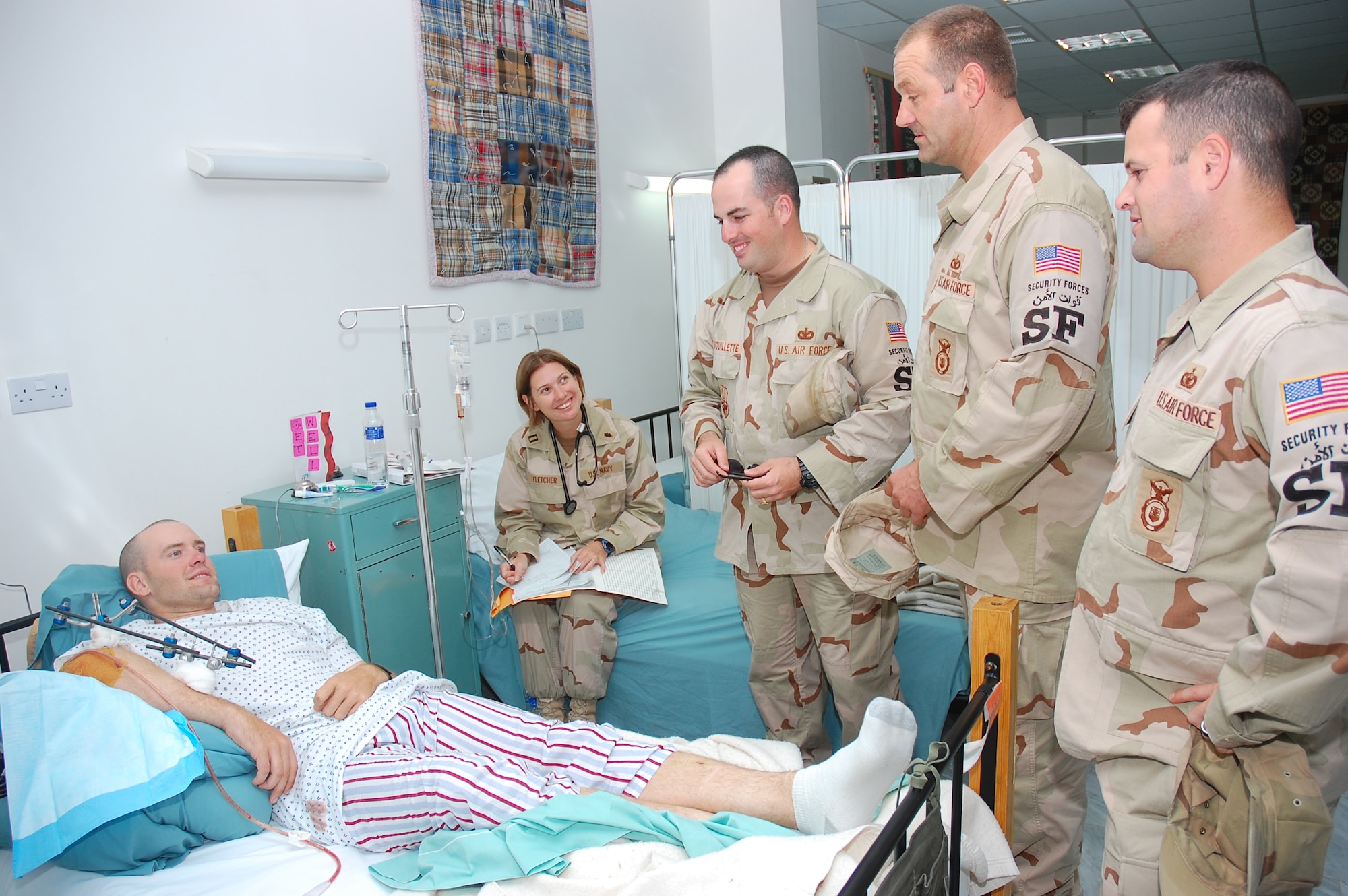 SOUTHWEST ASIA -- (L to R) Staff Sgt. Jason Brouillette, Tech. Sgt. Perry Adams and Staff Sgt. Richard Remington, 386th Expeditionary Security Forces Squadron, visit injured security forces comrade, Staff Sgt. Rick Adams, while Navy Lt. Wendy Fletcher, critical care nurse, goes through Sergeant Adams? medical documents, at the contingency aeromedical staging facility here Oct. 31.  Sergeant Adams, who is who is assigned to the 887th Expeditionary Security Forces Squadron and is deployed from Moody AFB., Ga., was injured by an improvised explosive device Oct. 29 near Camp Bucca, Iraq, and was also awarded the Purple Heart medal.  (U.S. Air Force photo by Staff Sgt. Tia Schroeder)