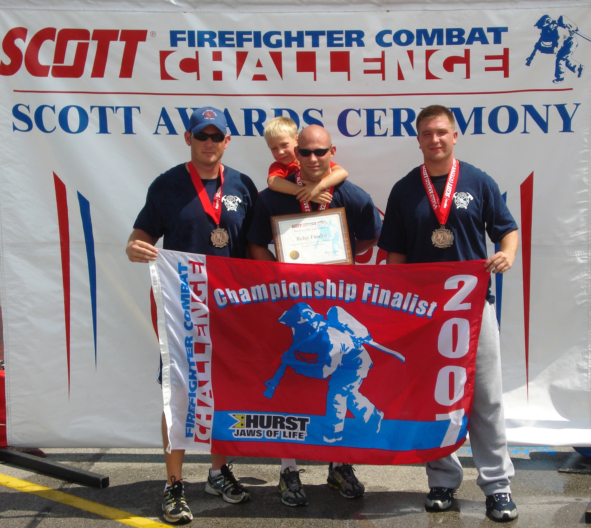 Left to right: Christopher Finkes, Staff Sgts. Cory McGee and Joshua Miller, all from the 509th Civil Engineer Squadron, and Ayden McGee, son of Sergeant McGee, display the Scott Firefighter Combat Challenge's finalist banner awarded to Sergeant McGee after he won the challenge in Omaha, Neb., Aug. 18-19. The firefighters, who comprise a three-man firefighting team from Whiteman, also represented the base the following weekend at Sioux Falls, S.D., Aug. 23-26. (Photo printed with permission of Staff Sgt. Joshua Miller)