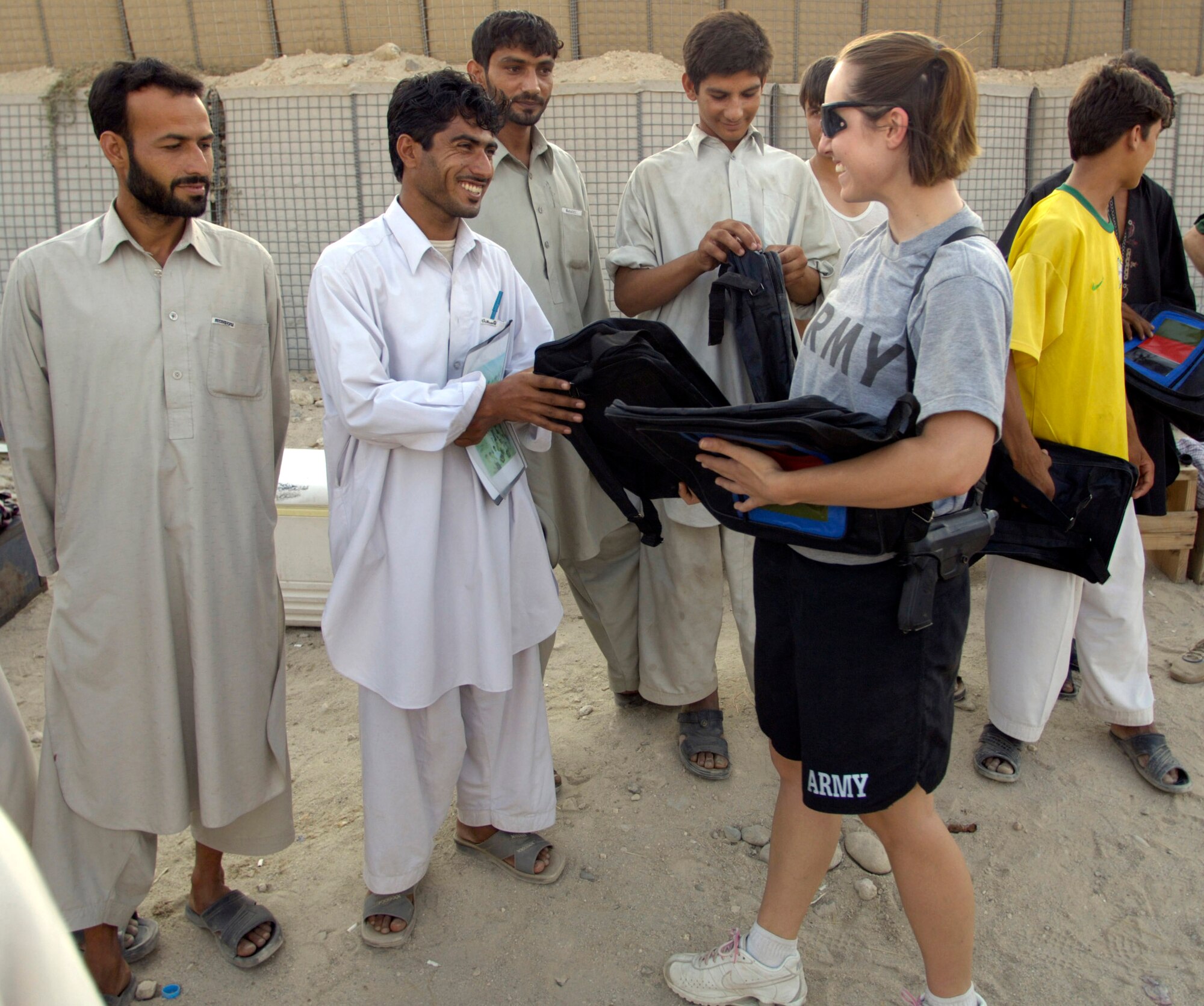 Army Sgt. Sam St. Pierre hands out book bags to the participants of a volleyball game hosted by Airmen and Soldiers Aug. 26 at Forward Operating Base Mehtar Lam, located in Afghanistan's Laghman Province. The weekly volleyball games are designed to bring area high school students from the province's five districts to the base to meet and interact with military members in a friendly atmosphere. Sergeant St. Pierre is a Provincial Reconstruction Team member and Army civil affairs specialist. (U.S. Air Force photo/Master Sgt. Jim Varhegyi) 
