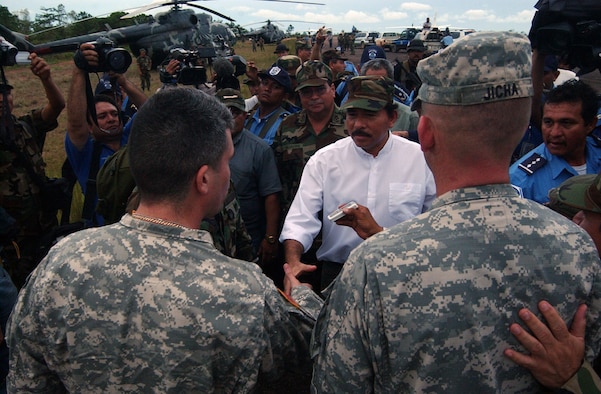 PUERTO CABEZAS, Nicaragua -- Army Capt. Jon-Paul Lavandeira (left) and Lt. Col. Gregory Jicha, both assigned to Joint Task Force-Bravo at Soto Cano Air Base, Honduras, greet Nicaraguan President Daniel Ortega among a media frenzy after arriving at a small airfield here Sept. 5.  The Army officers are part of a 13-person task force that deployed here to assess damage from the storm.  US Air Force photo by Tech. Sgt. Sonny Cohrs                              