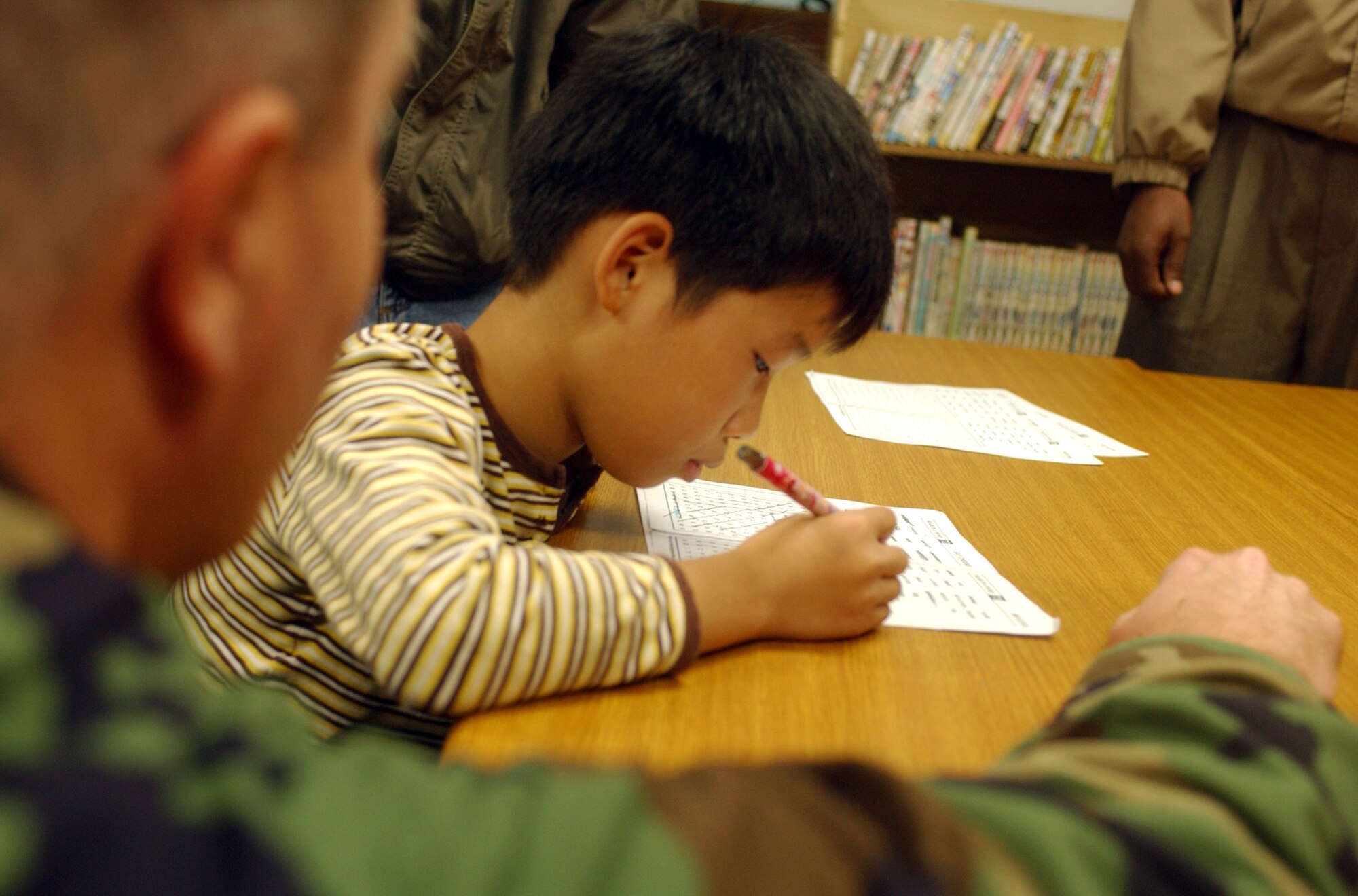 Gunsan City, South Korea -- A child searches for a word during his English class as Maj. Richard Fitzgerald, 8th Fighter Wing Chaplain, assists at the Gunsan Orphanage here Sept. 5.  The 8th Logistics Readiness Squadron volunteered at the Kunsan Air Base Commissary to raise money for the children at the Gunsan Orphanage as part of a Good Neighbor Program initiative. After presenting the money, they spent time with the children.  (U.S. Air Force photo/Senior Airman Steven R. Doty)                                